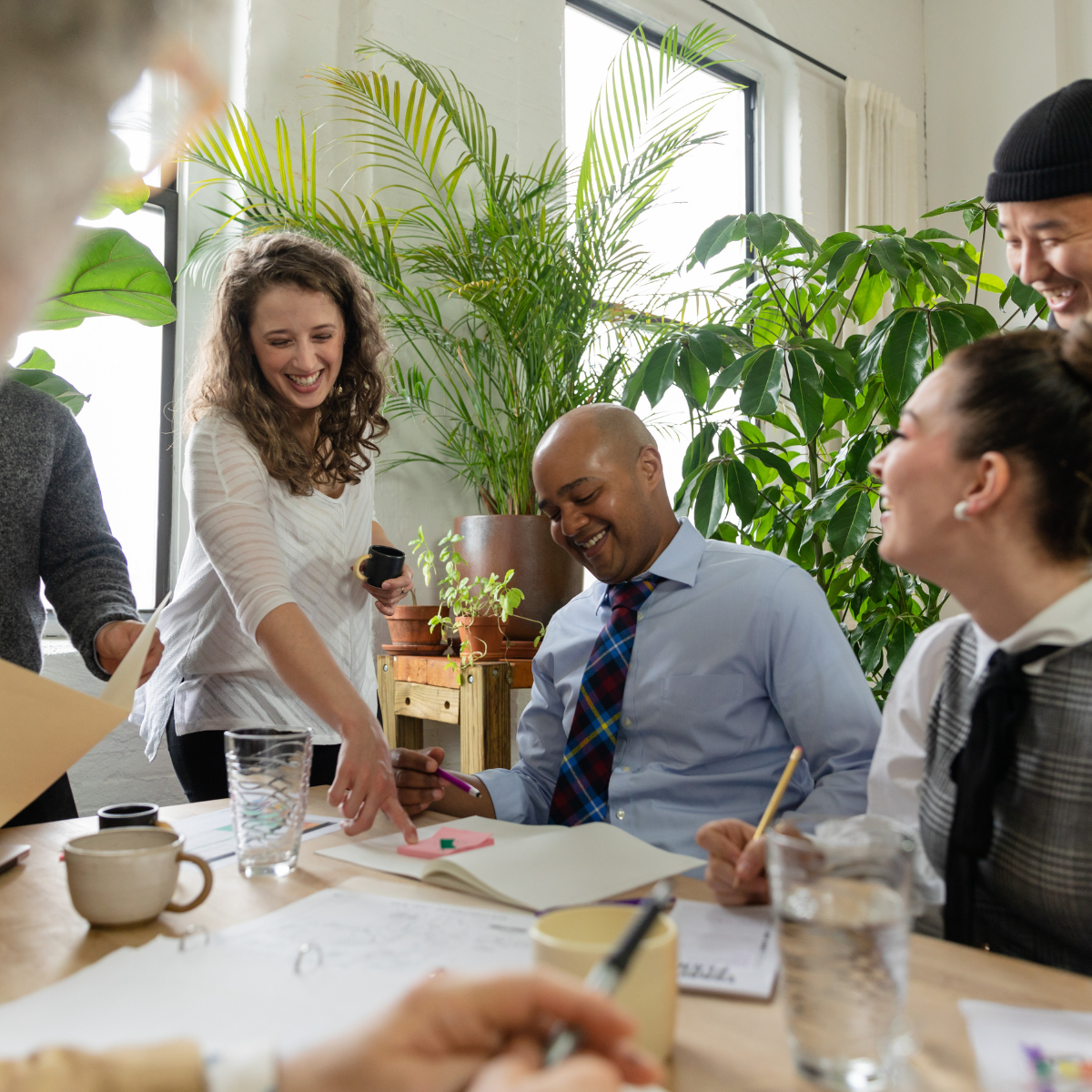 A group of people are sitting around a table with plants in the background