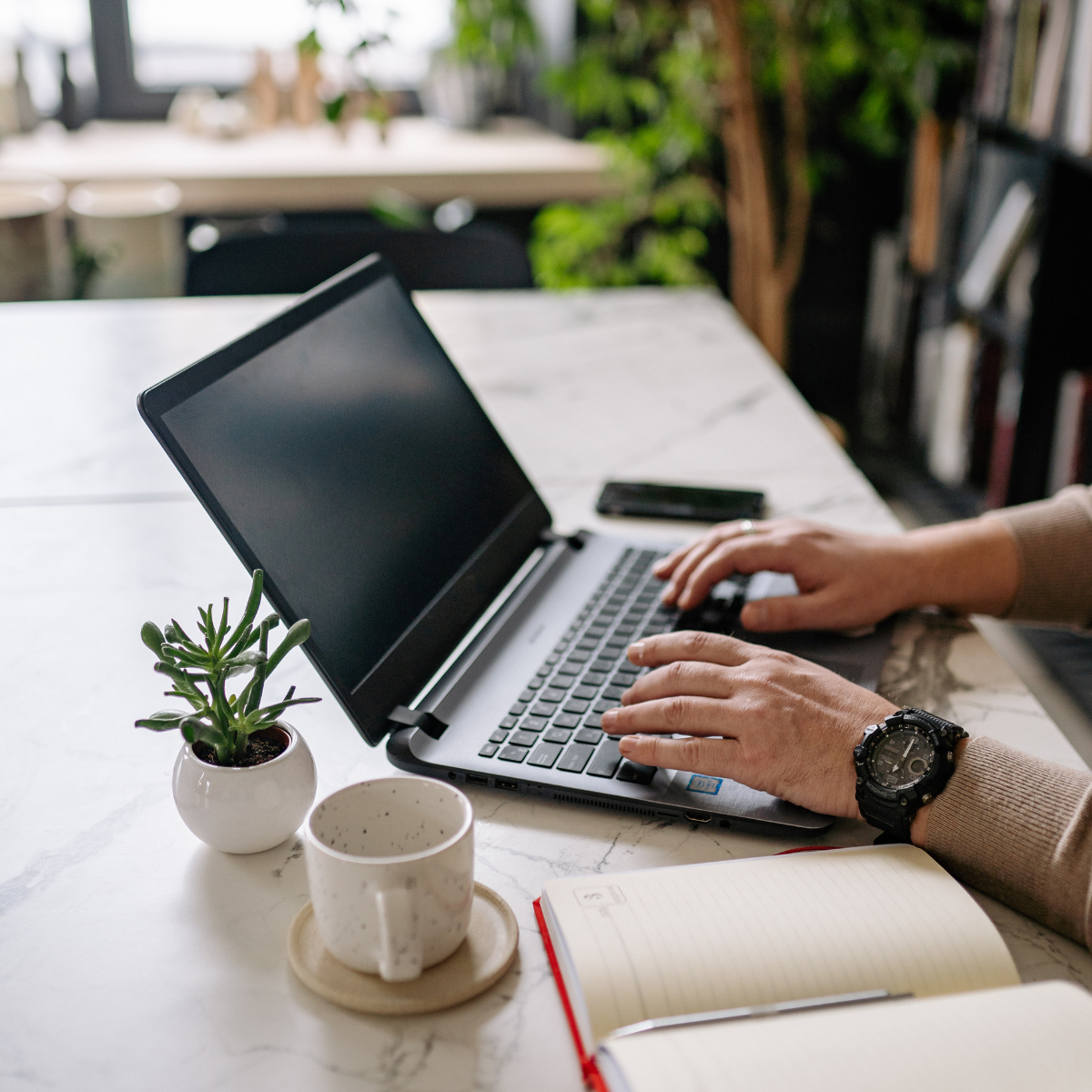 A person is typing on a laptop computer while wearing a watch.
