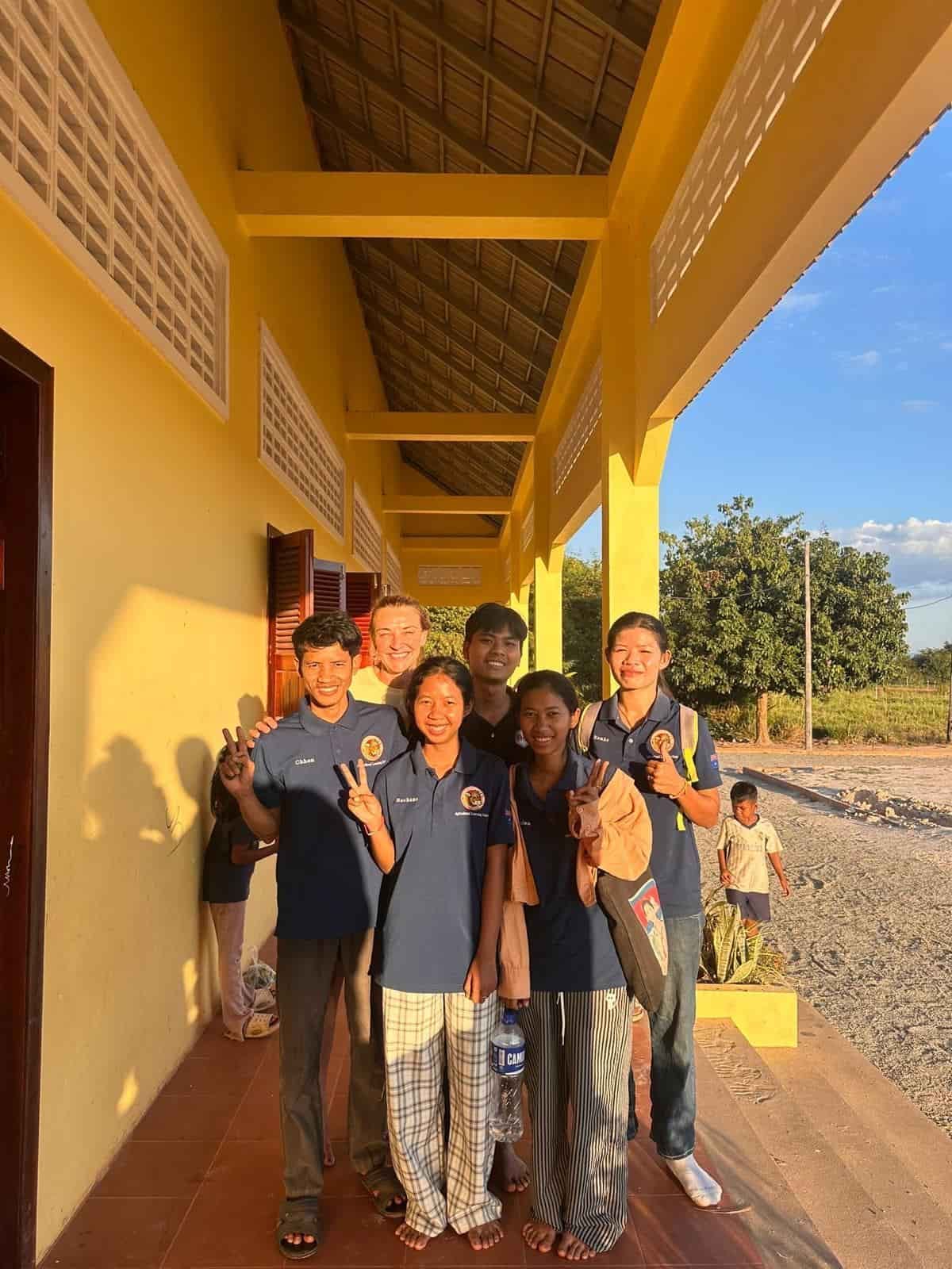 Group of people smiling, standing on a yellow porch; some wear matching blue shirts.