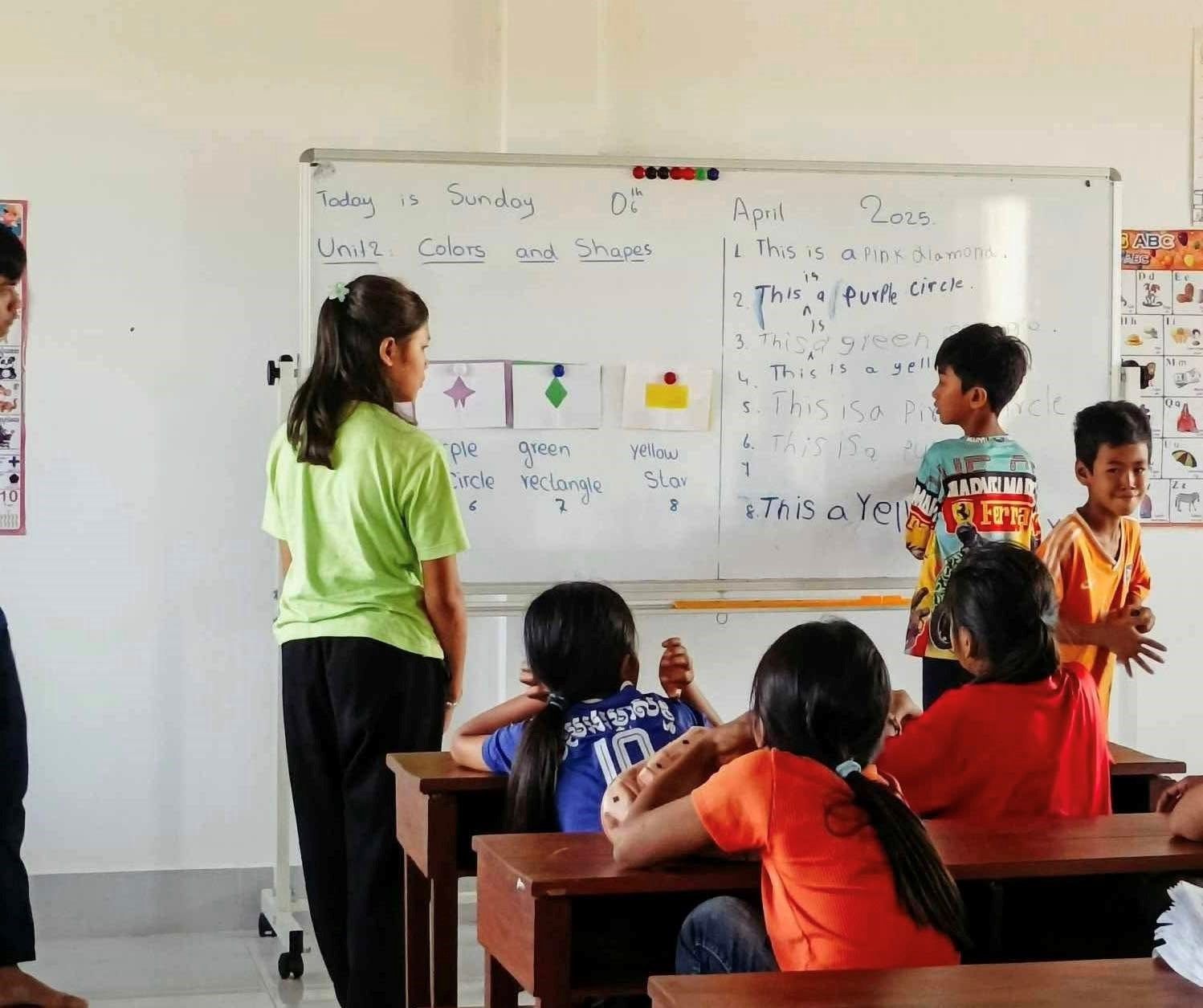 A group of children are sitting at desks in a classroom in front of a white board