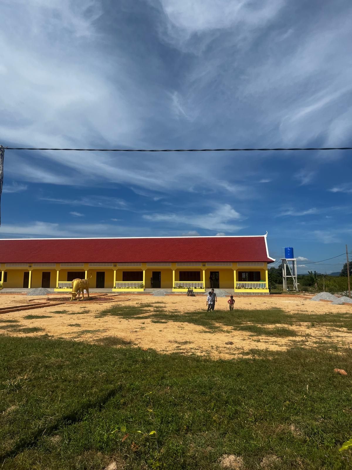 A yellow building with a red roof is sitting in the middle of a grassy field.