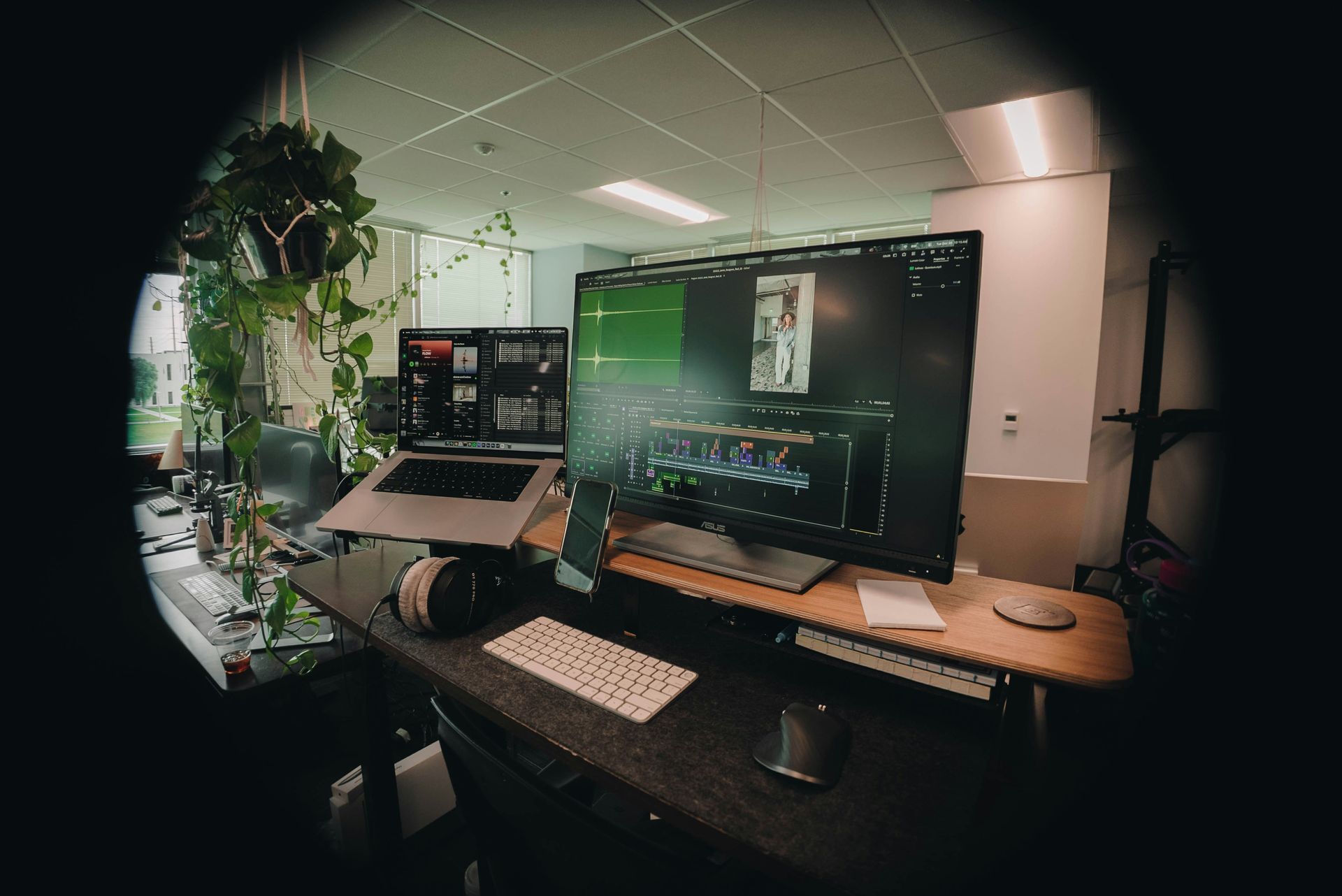 Desk with computer monitors, keyboard, headphones, and plants. Editing workspace.