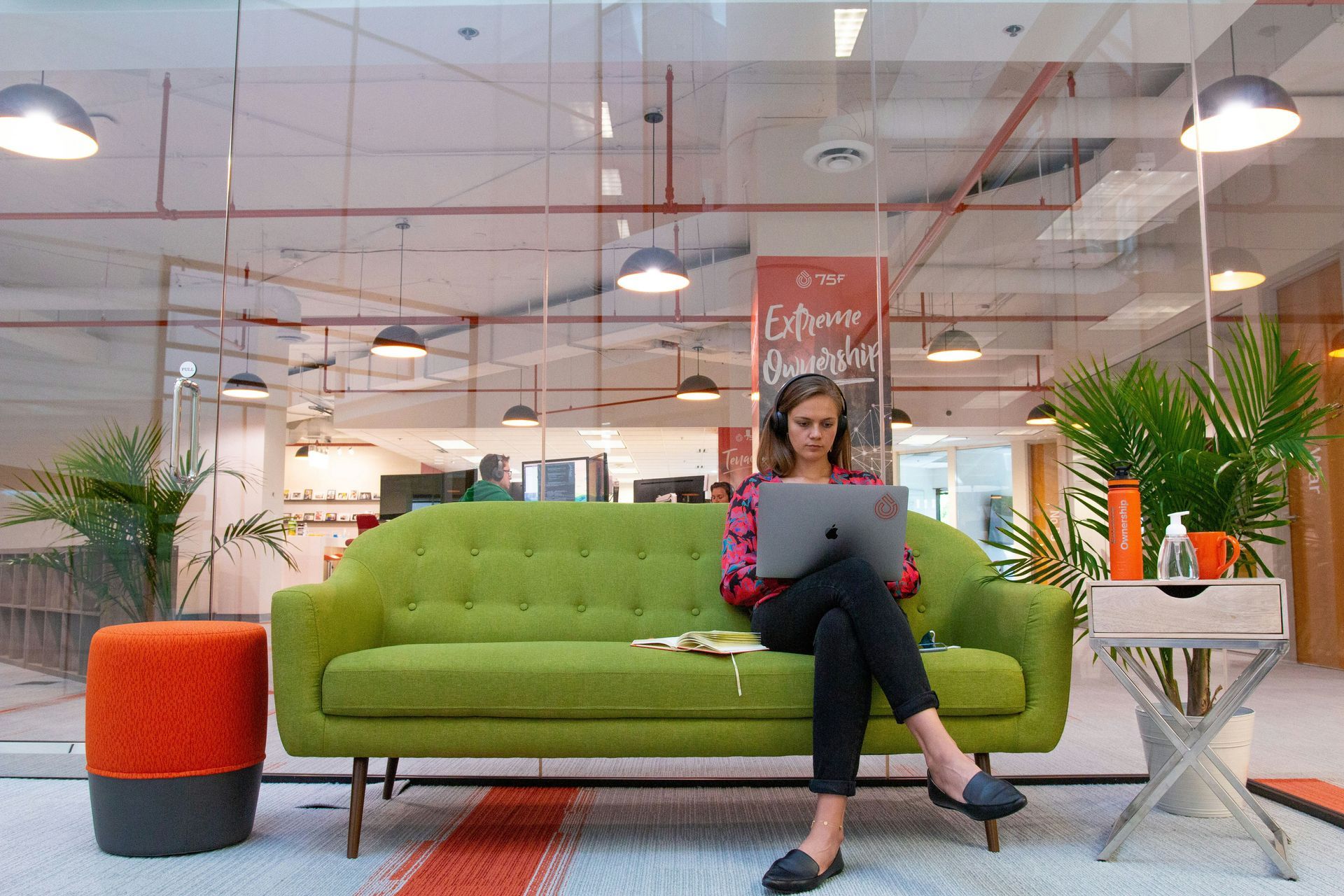 A woman is sitting on a green couch using a laptop computer.
