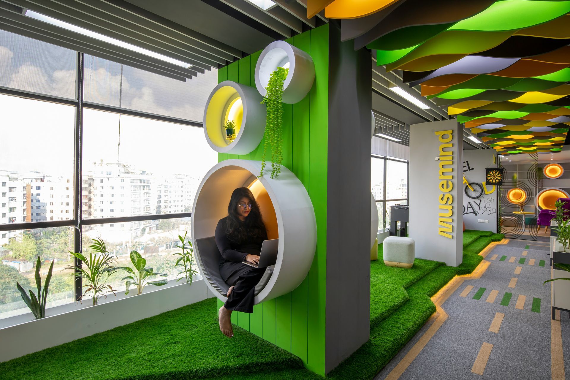 Woman in a modern office seating area with a green and yellow theme, sitting in a circular pod.
