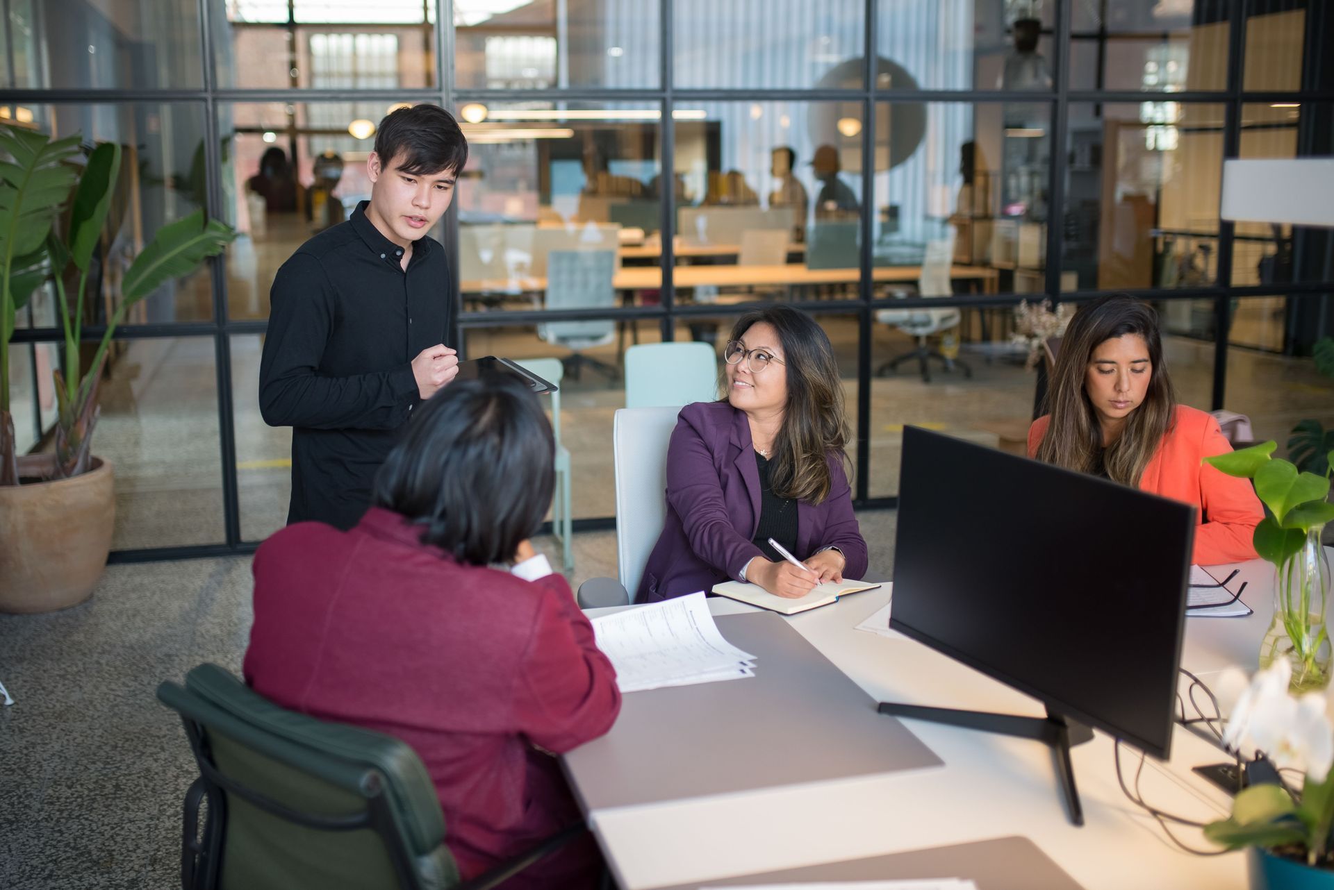 Group of people collaborating around a table with notebooks, tablets, and colorful office supplies