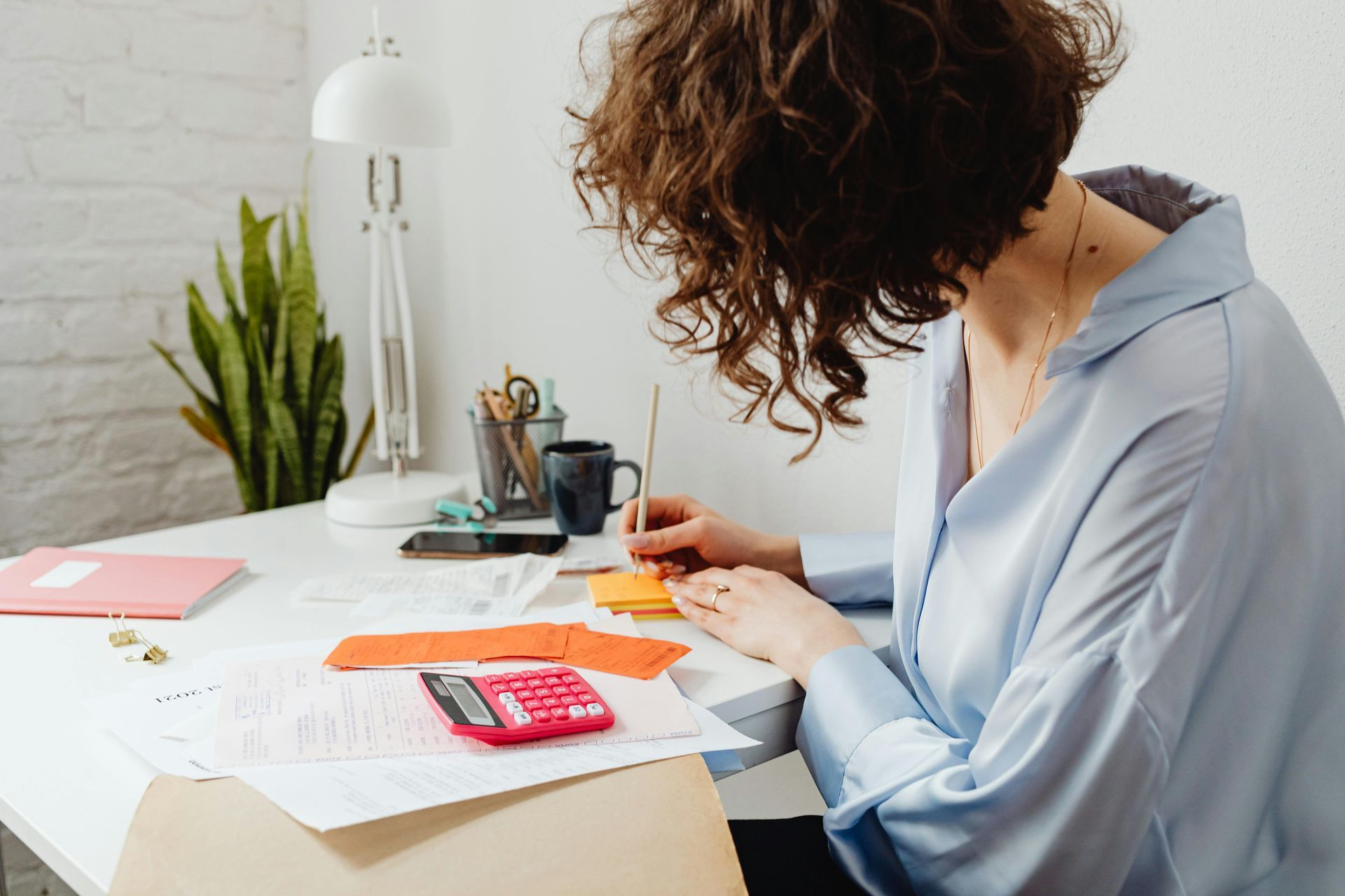 A woman is sitting at a desk with a calculator and a pen.