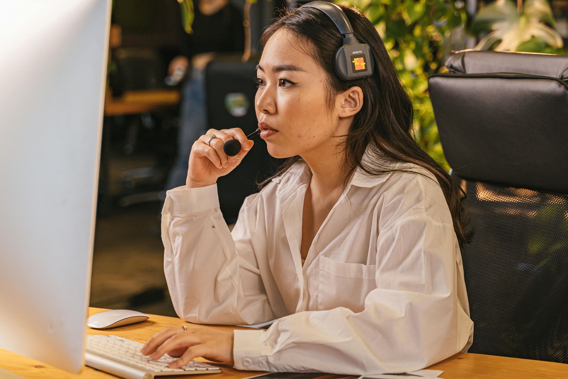 Woman wearing a headset and typing at a computer in an office setting. She is focused, and the background is blurred.