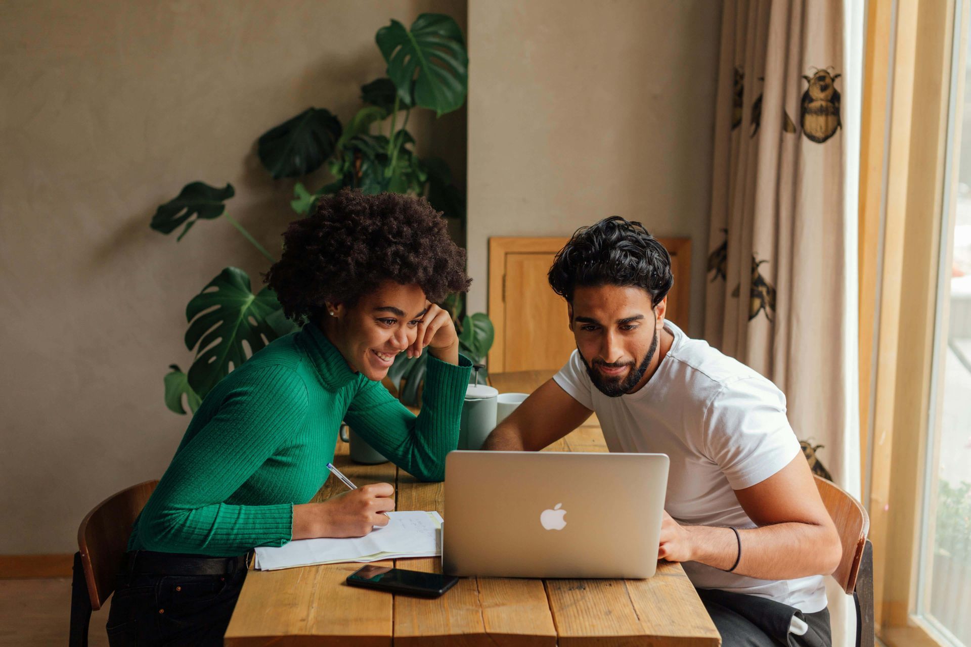 A man and a woman are sitting at a table looking at a laptop.