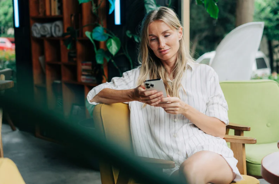 Blonde woman in white shirt sits, using a phone, in a cafe with green and yellow furniture.