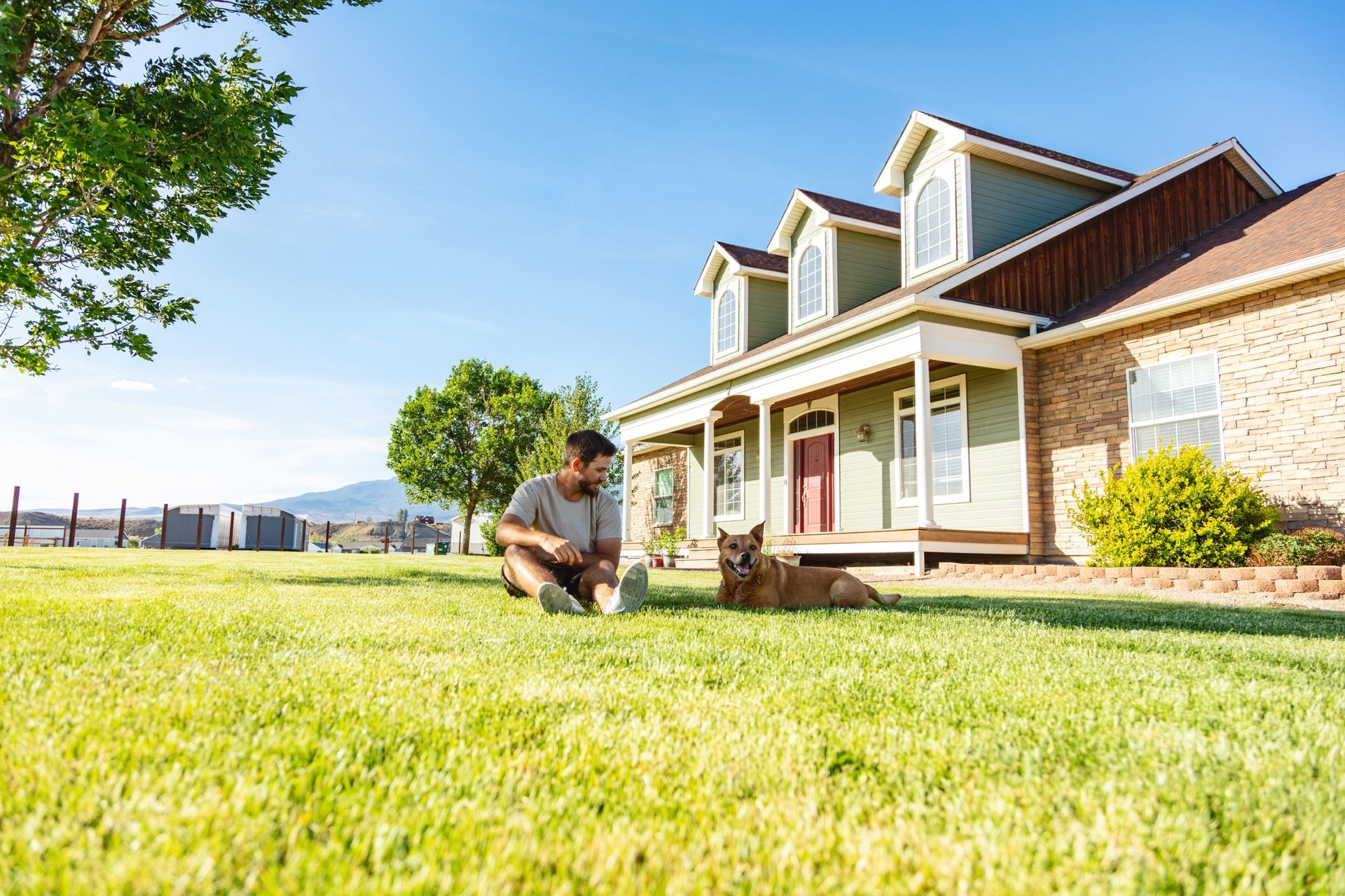 a man is kneeling in the grass next to a dog in front of a house .