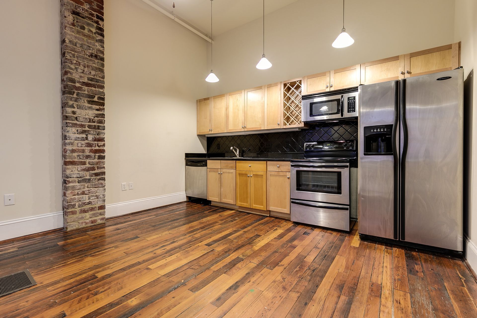 Kitchen with wood floors, stainless steel appliances, exposed brick column, and light wood cabinets.