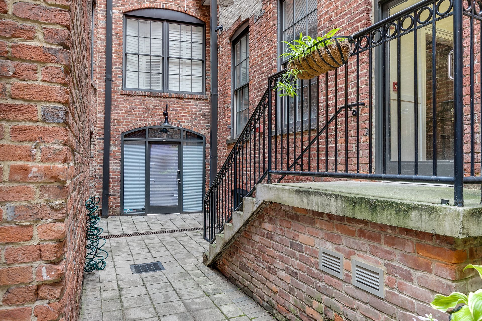 Brick courtyard with stairs and wrought iron railing leading to doorways.