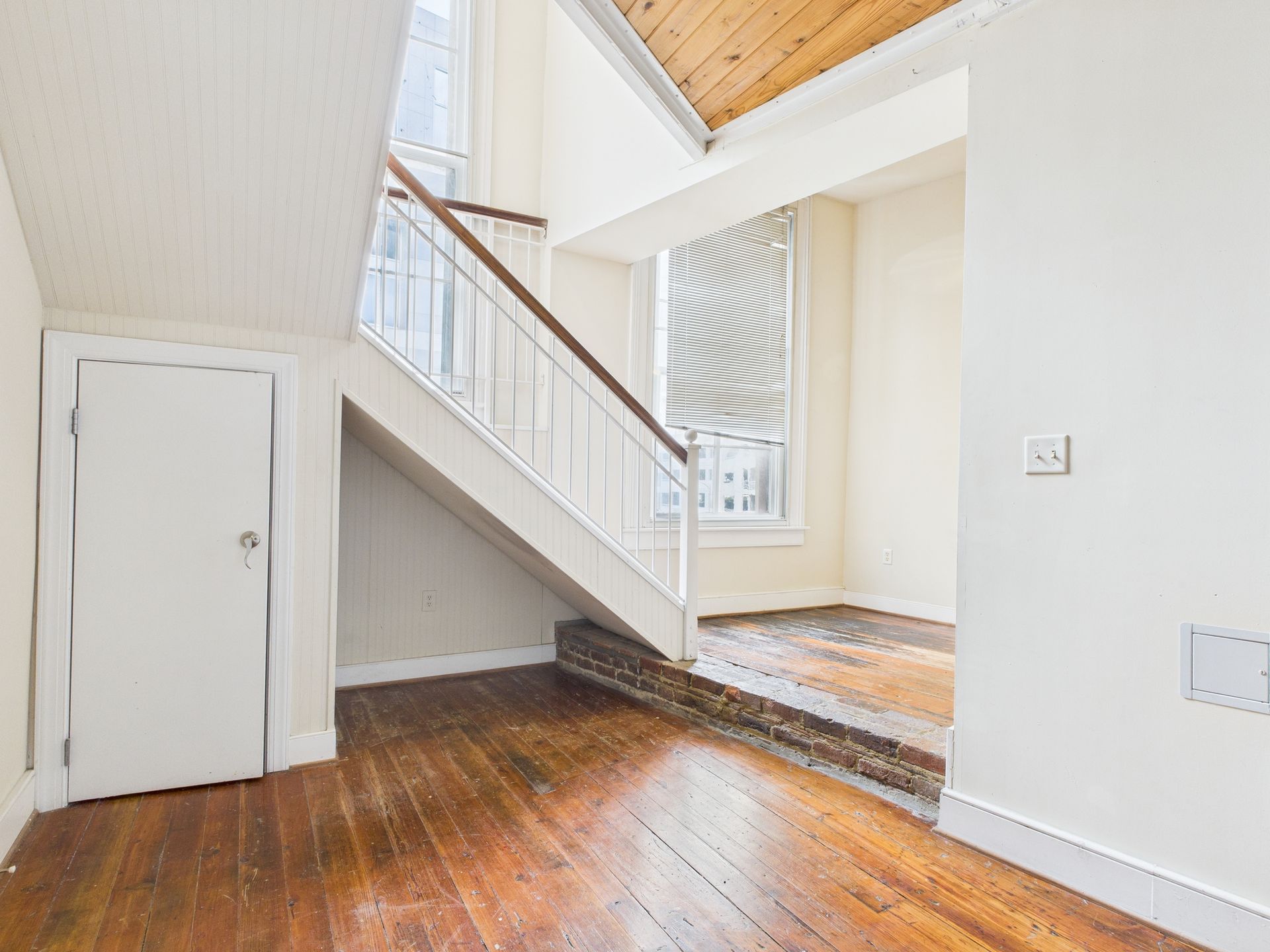 Wooden staircase in a home with hardwood floors, a white door, and windows.