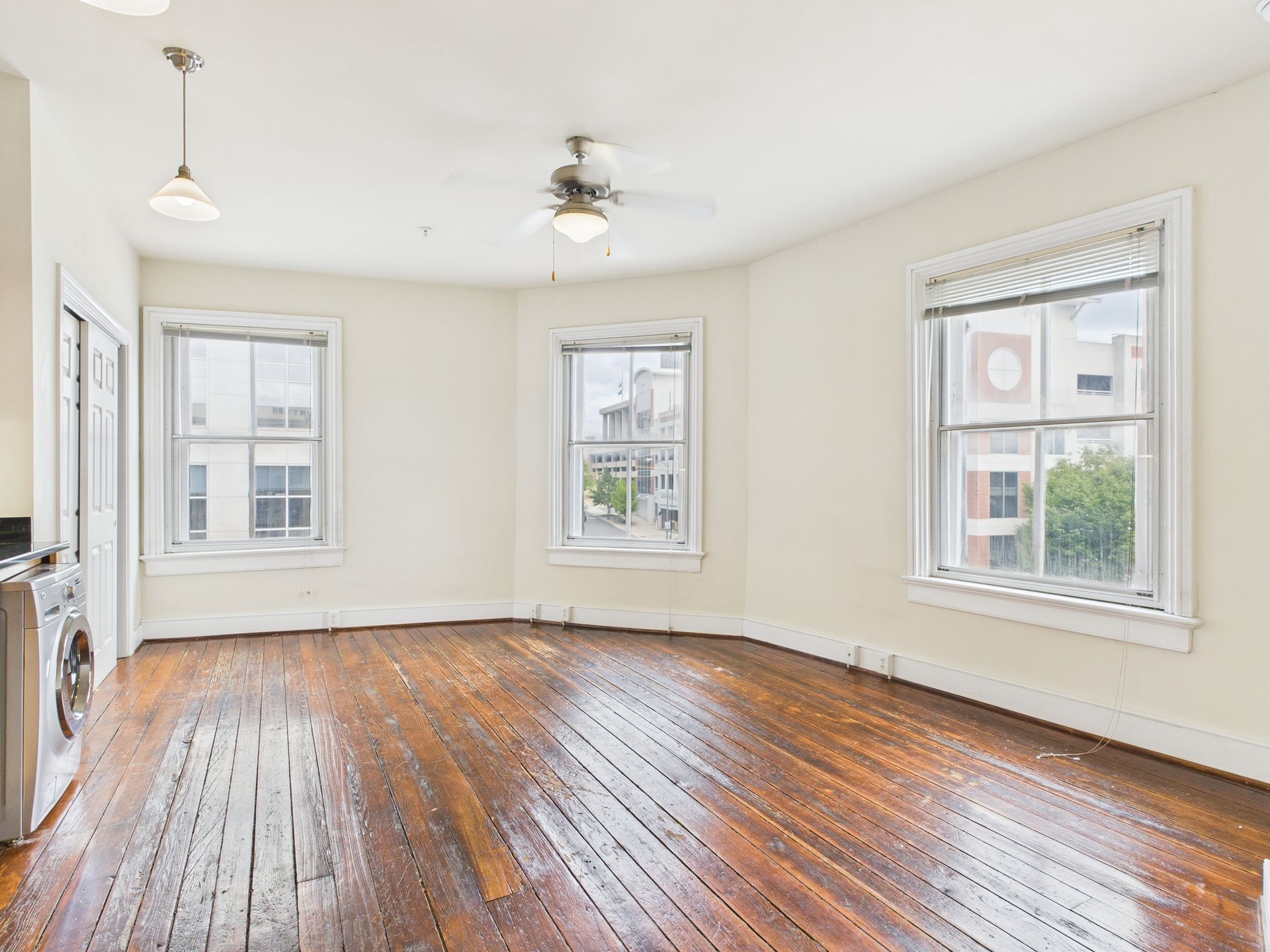 Empty room with hardwood floors, windows, and white walls.