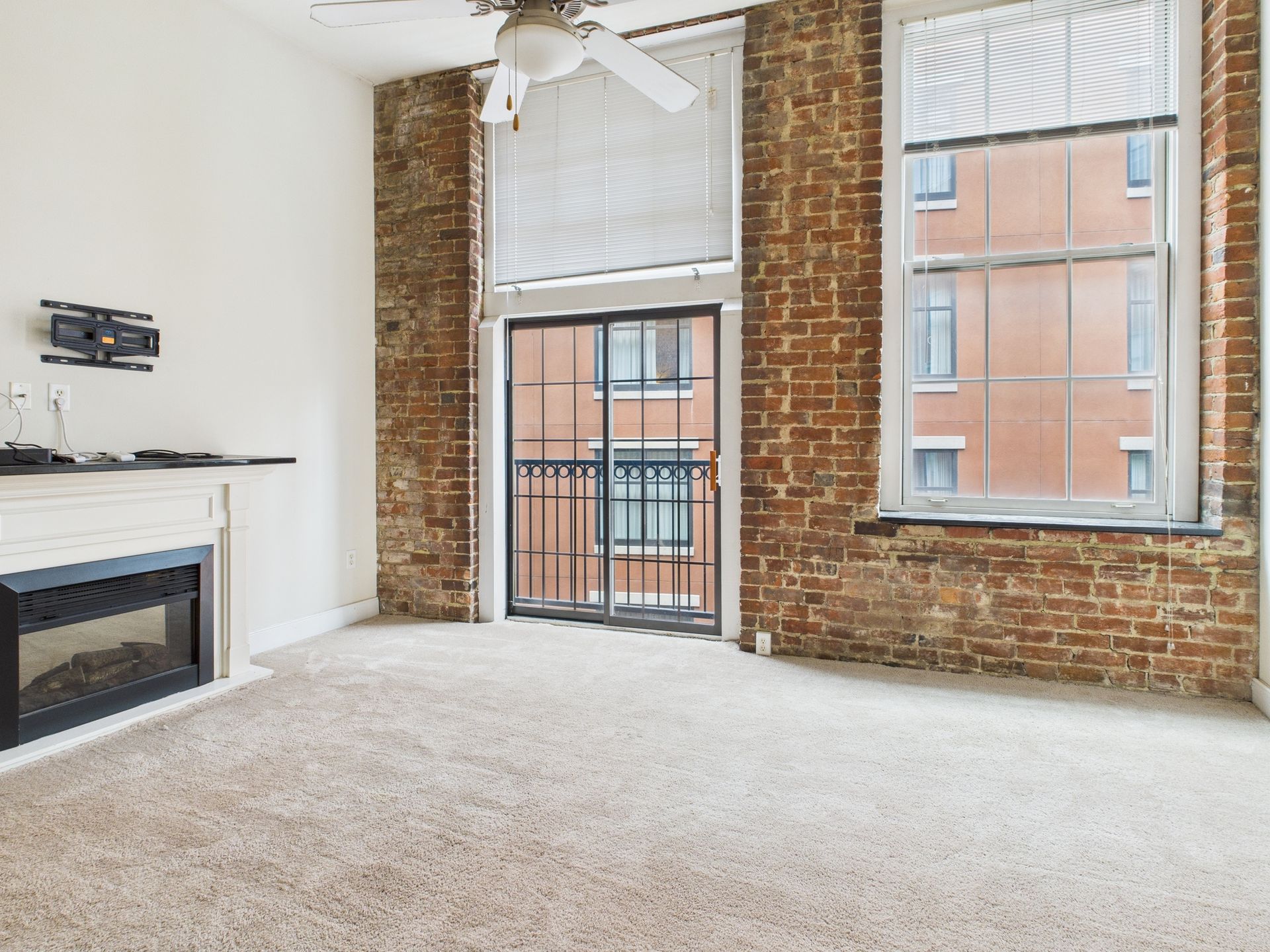 Empty room with carpet, exposed brick walls, fireplace, and balcony door.