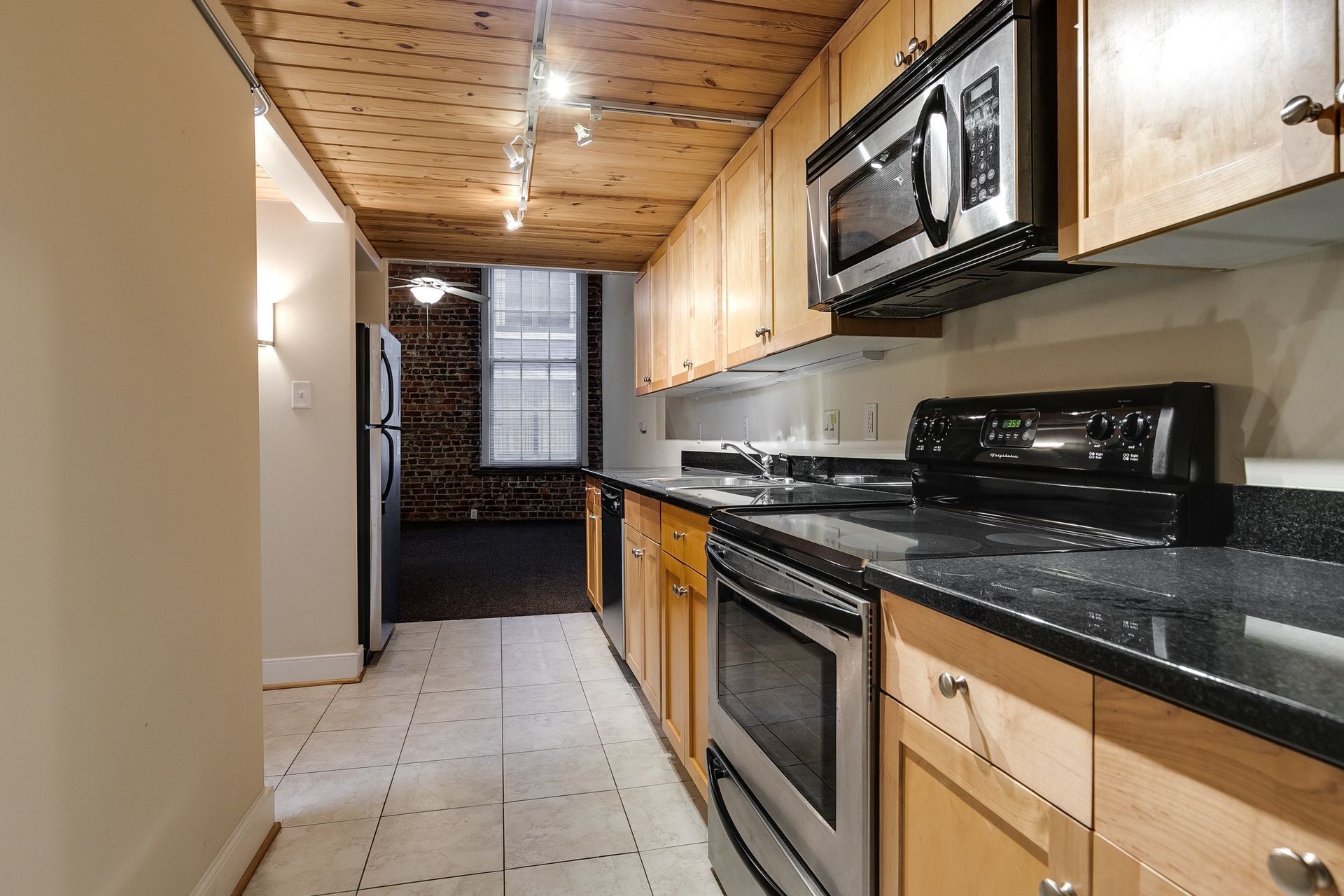 Kitchen with stainless steel appliances, light wood cabinets, dark countertops, and wood ceiling.