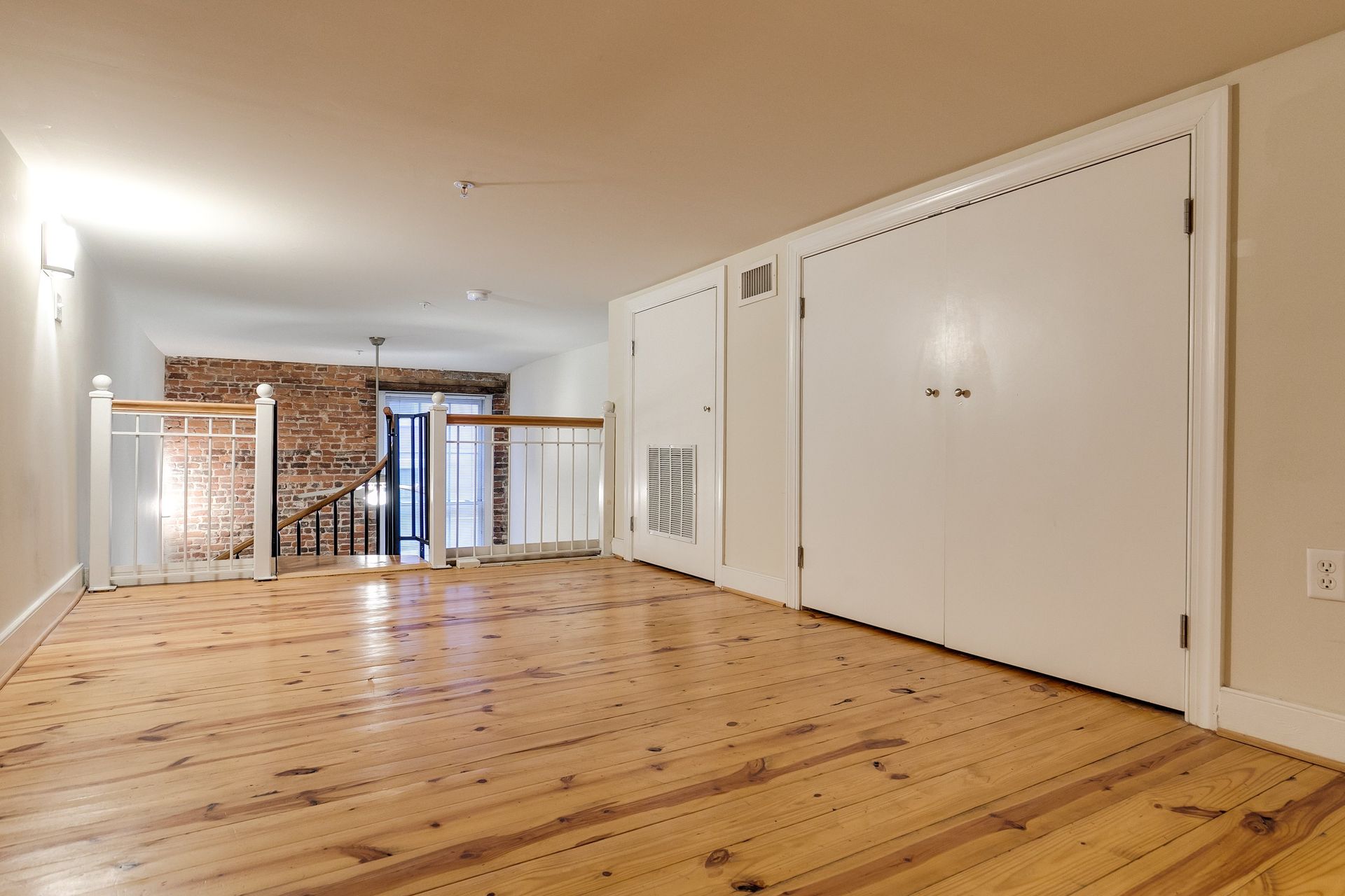 Loft interior with hardwood floors, white closet doors, and a brick wall visible.