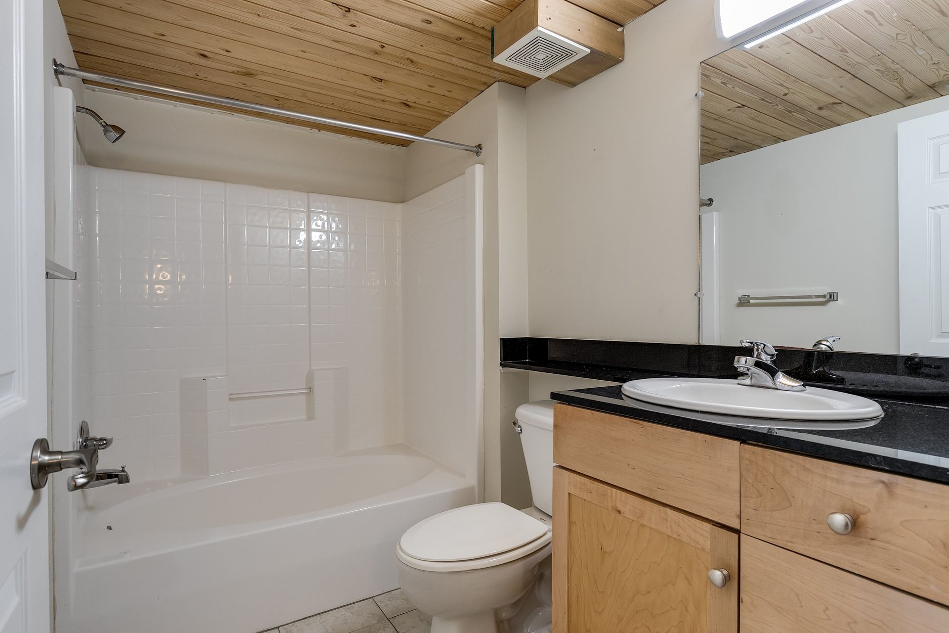 Bathroom with a white tub and toilet, light wood vanity, and a wood ceiling.