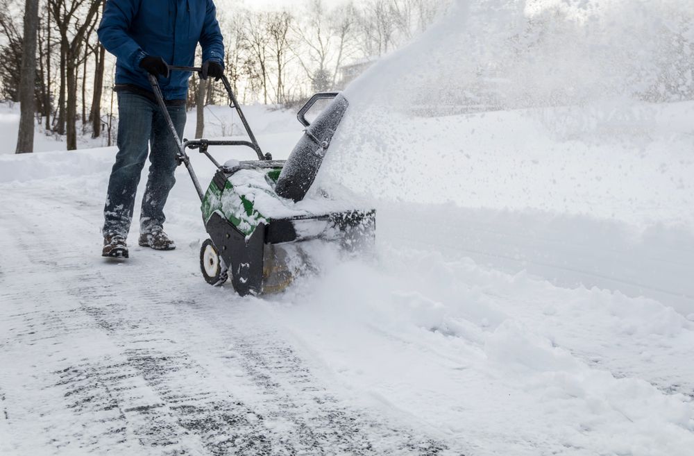 A man is using a snow blower to remove snow from a sidewalk.