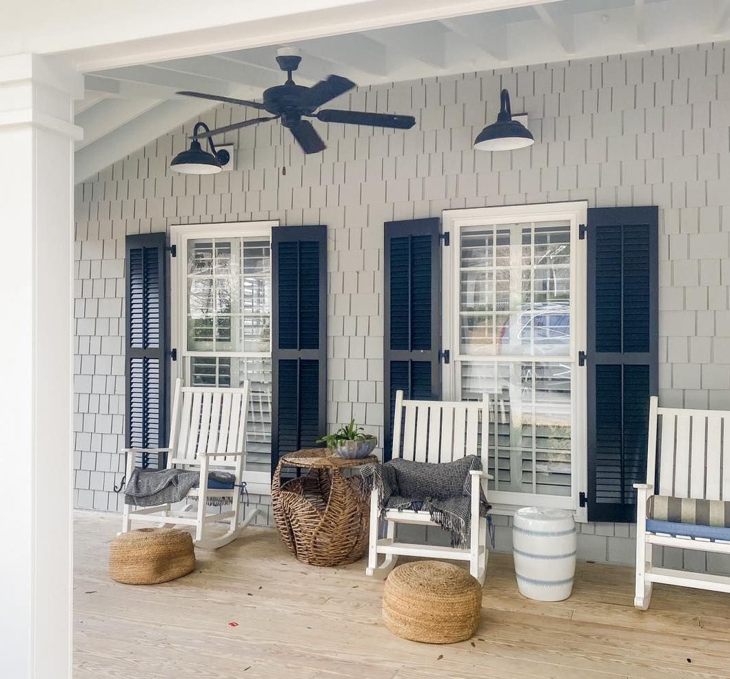 A porch with white rocking chairs, navy shutters, and wicker accents.