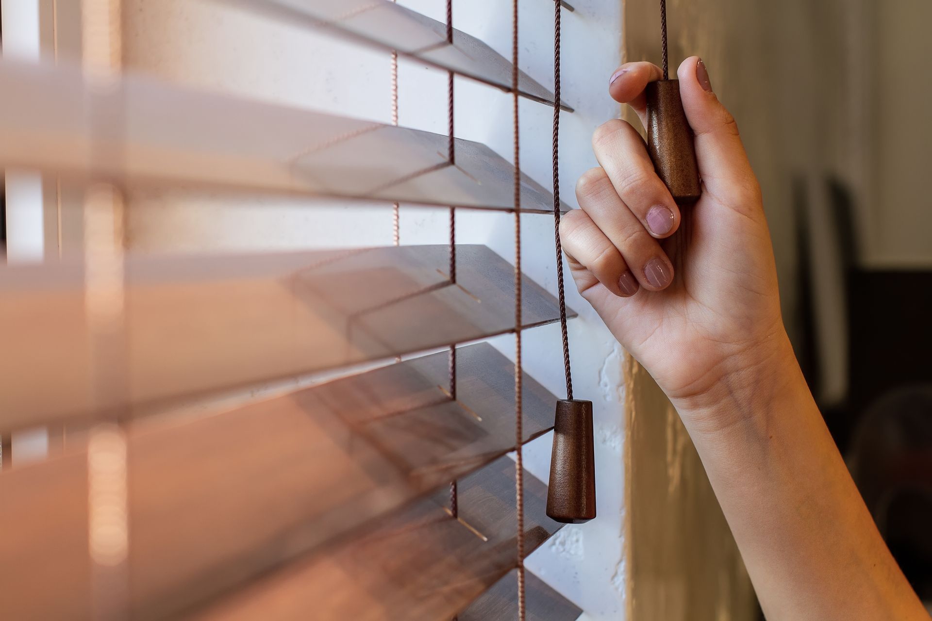 Hand adjusting premium wooden window blinds to control natural light in a modern home. Hand adjusting premium wooden window blinds to control natural light in a modern home.