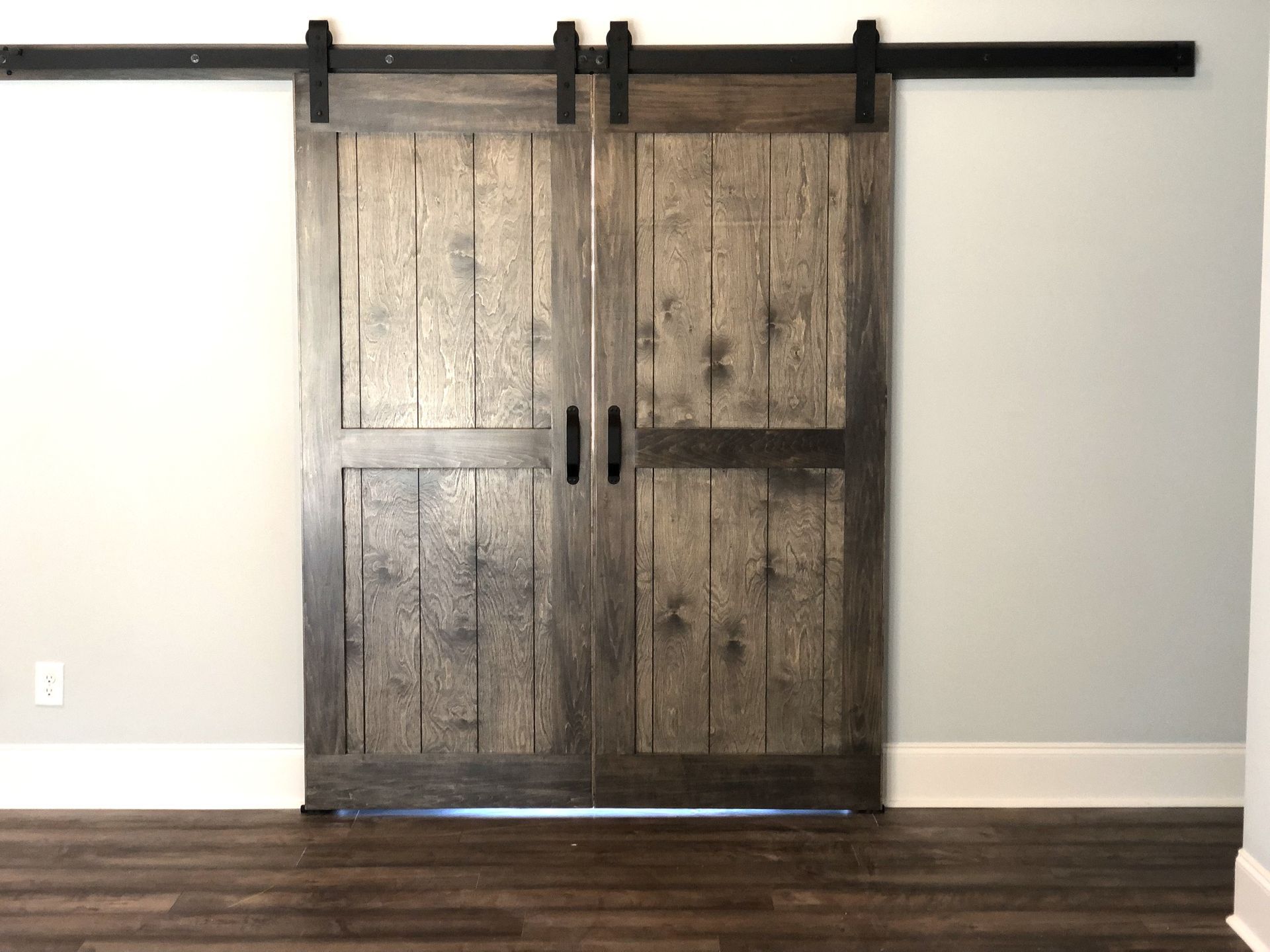 Double rustic barn doors, brown and black, with a black sliding rail, on a light gray wall.