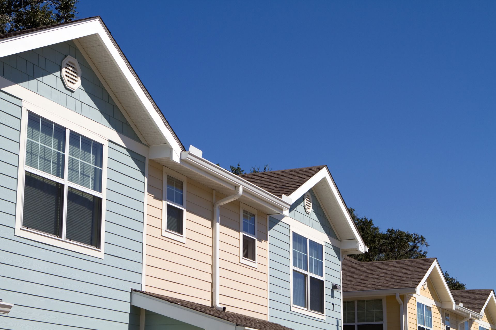 Side picture of an apartment with small windows with white frames, with the blue sky as background.