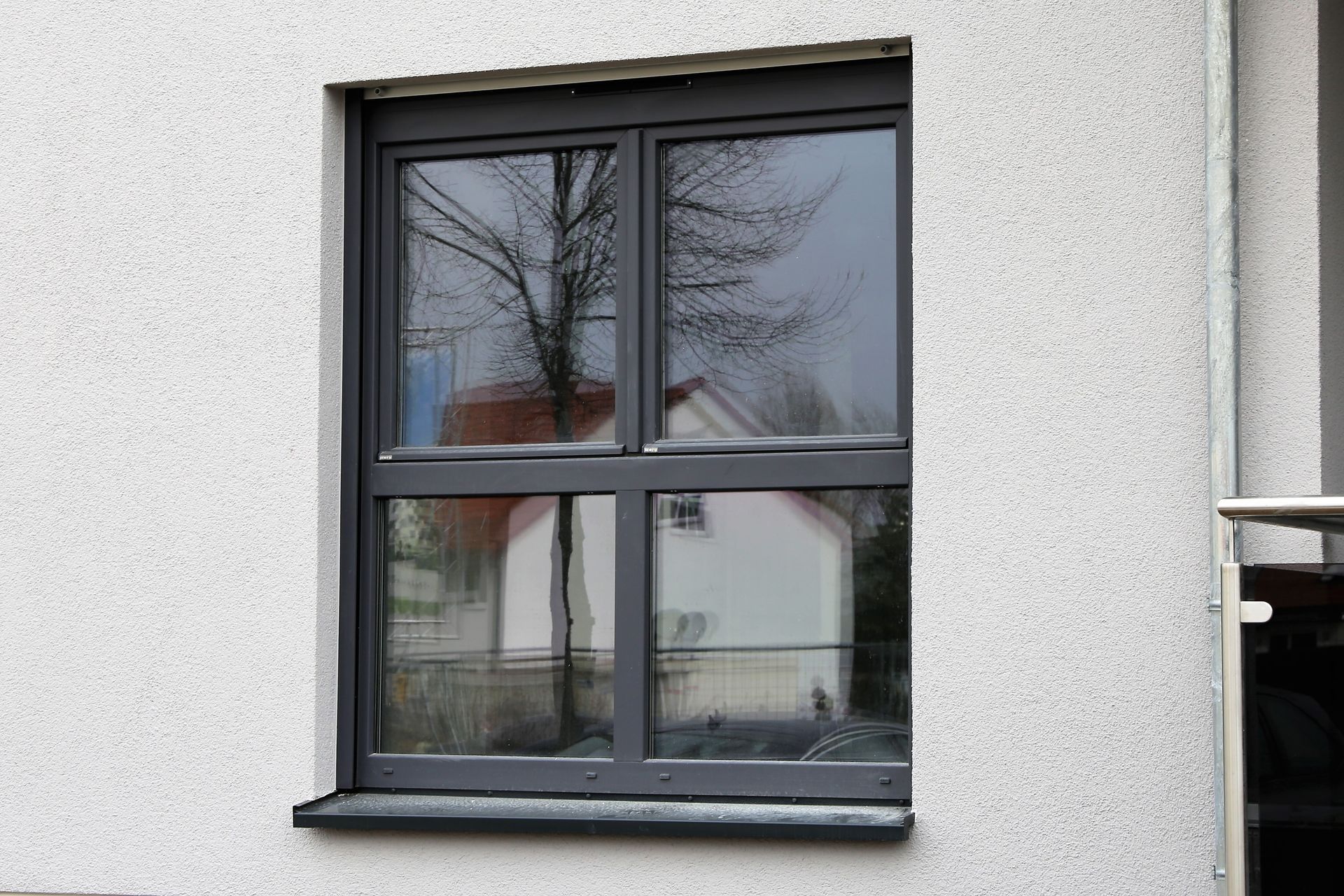 Exterior shot of a window with a black frame, on a white and textured wall