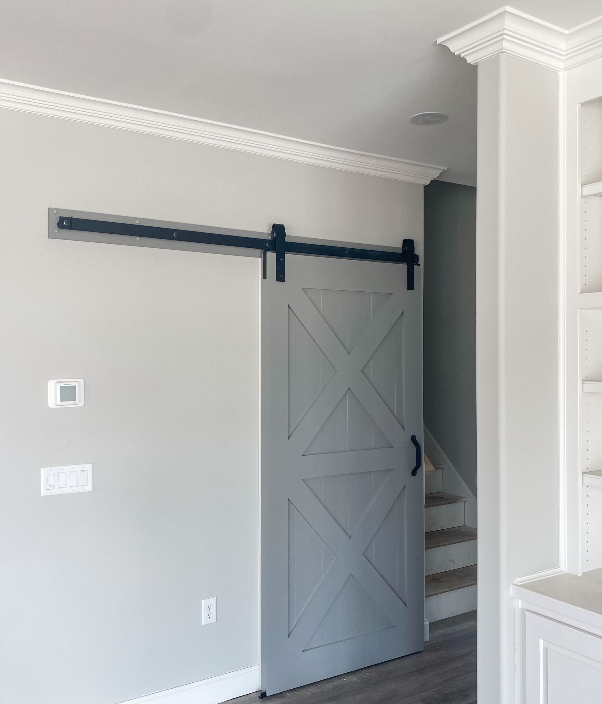 Gray barn door on a black track against a gray wall, leading to stairs.
