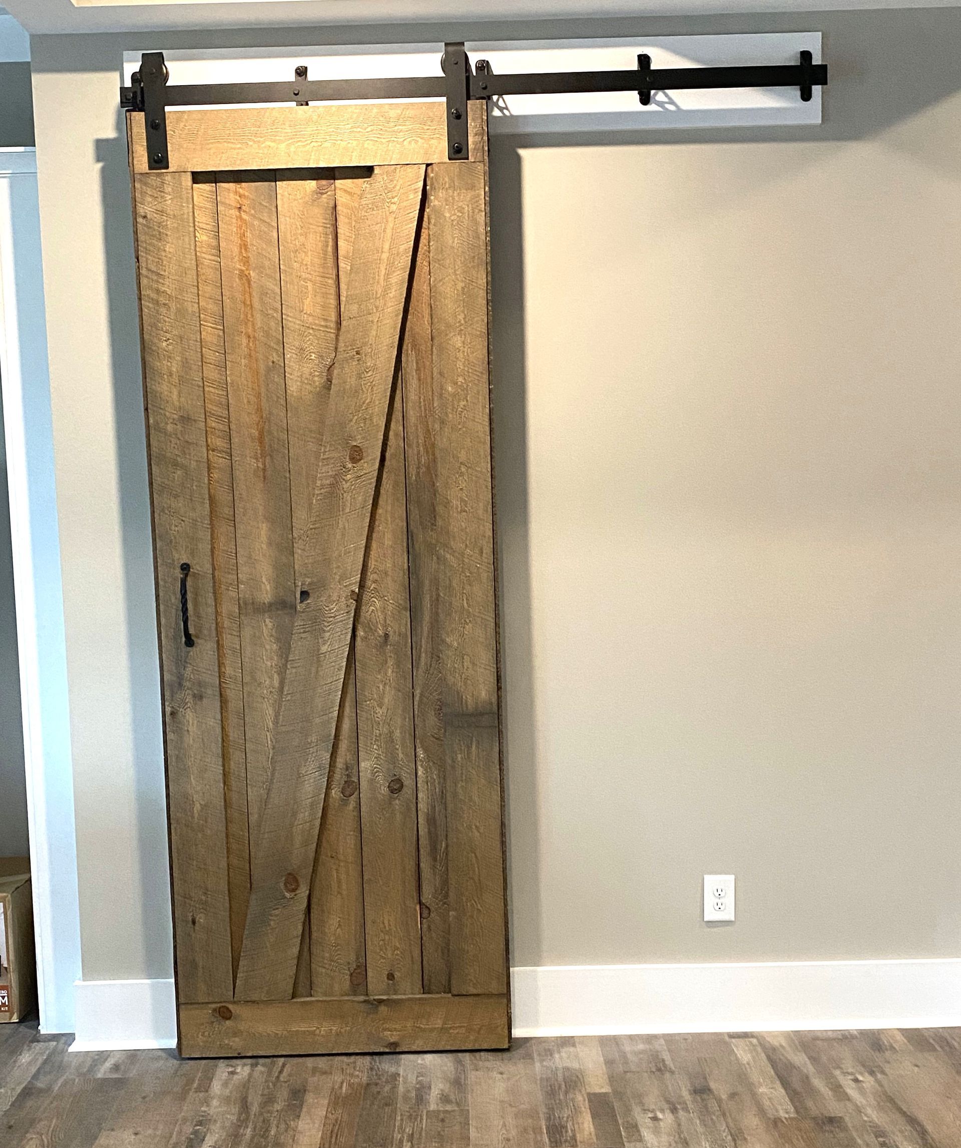 Barn door on sliding track against a beige wall, wooden floor.