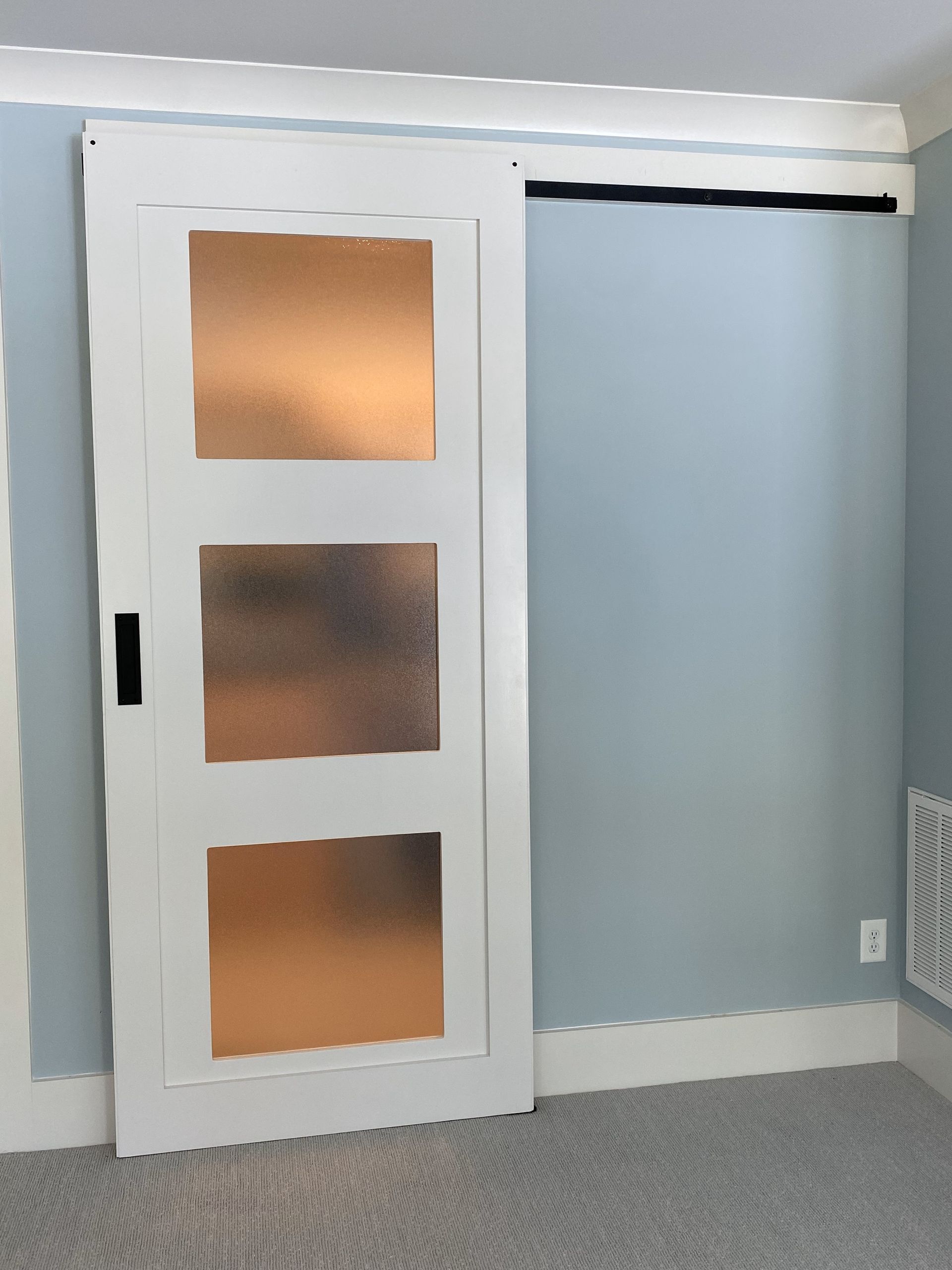 White sliding door with frosted glass panels on blue wall, black track.
