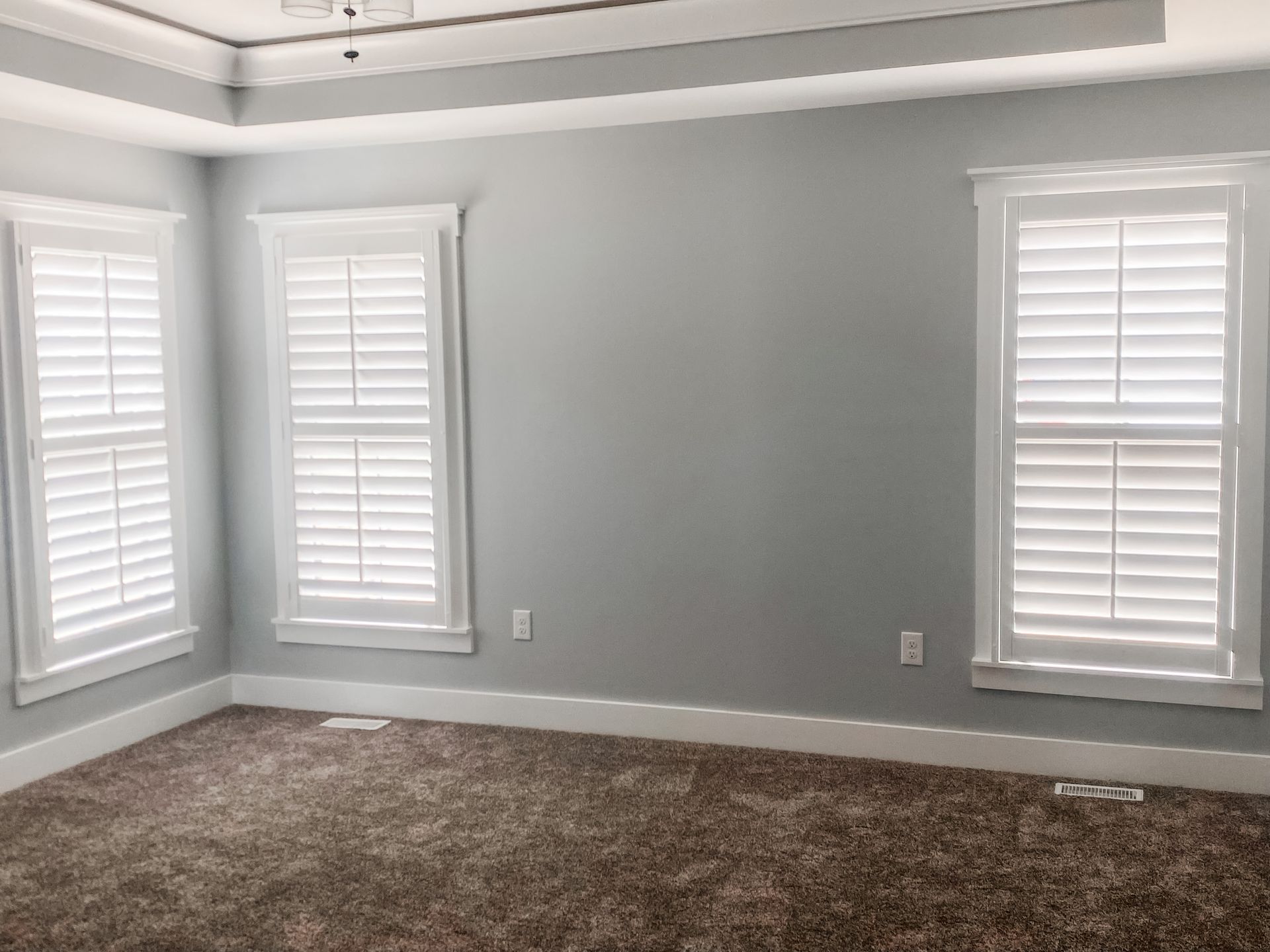 Empty bedroom with gray walls, white shutters, and brown carpet.