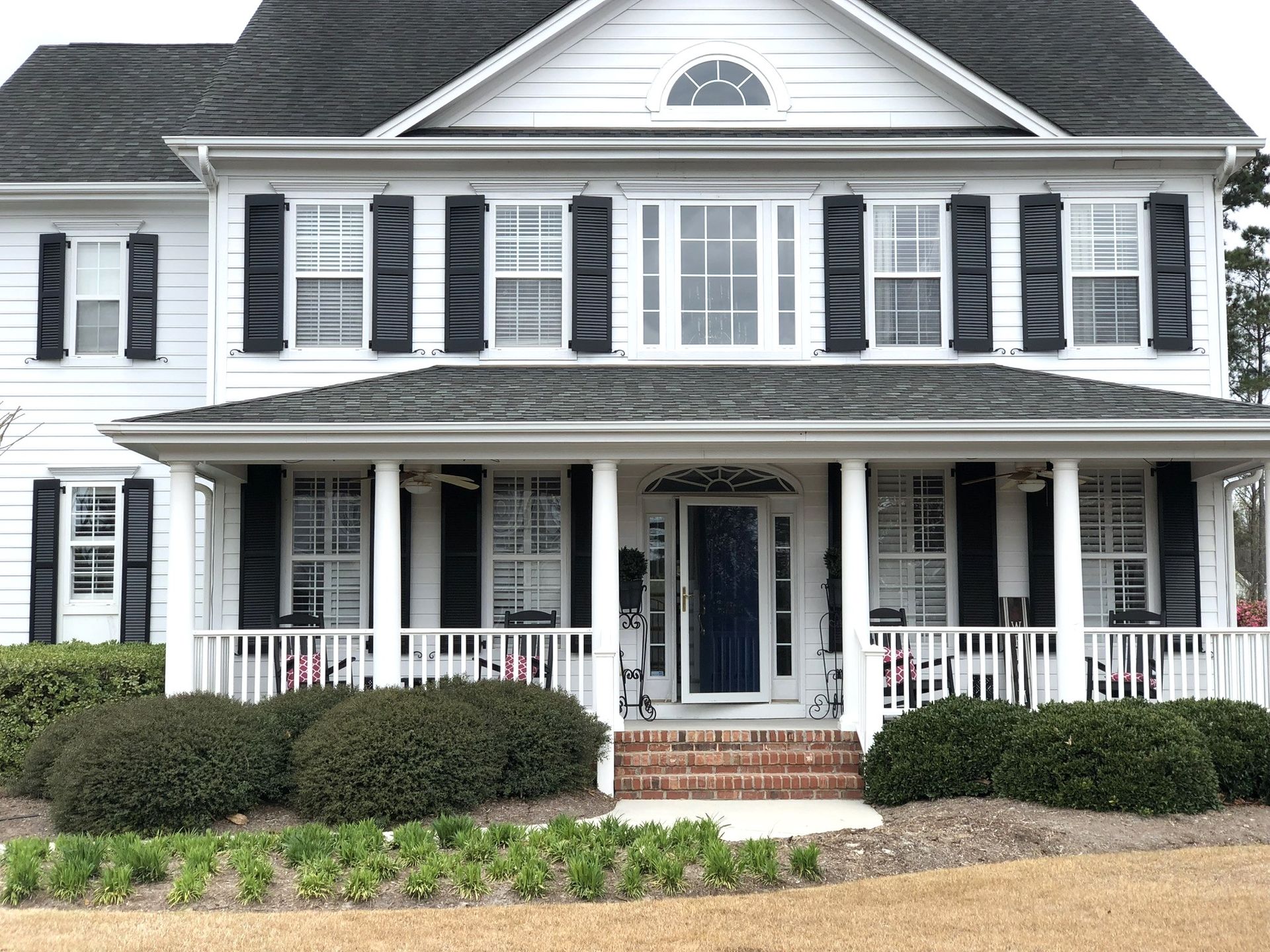 White house with black shutters, porch, and landscaping.