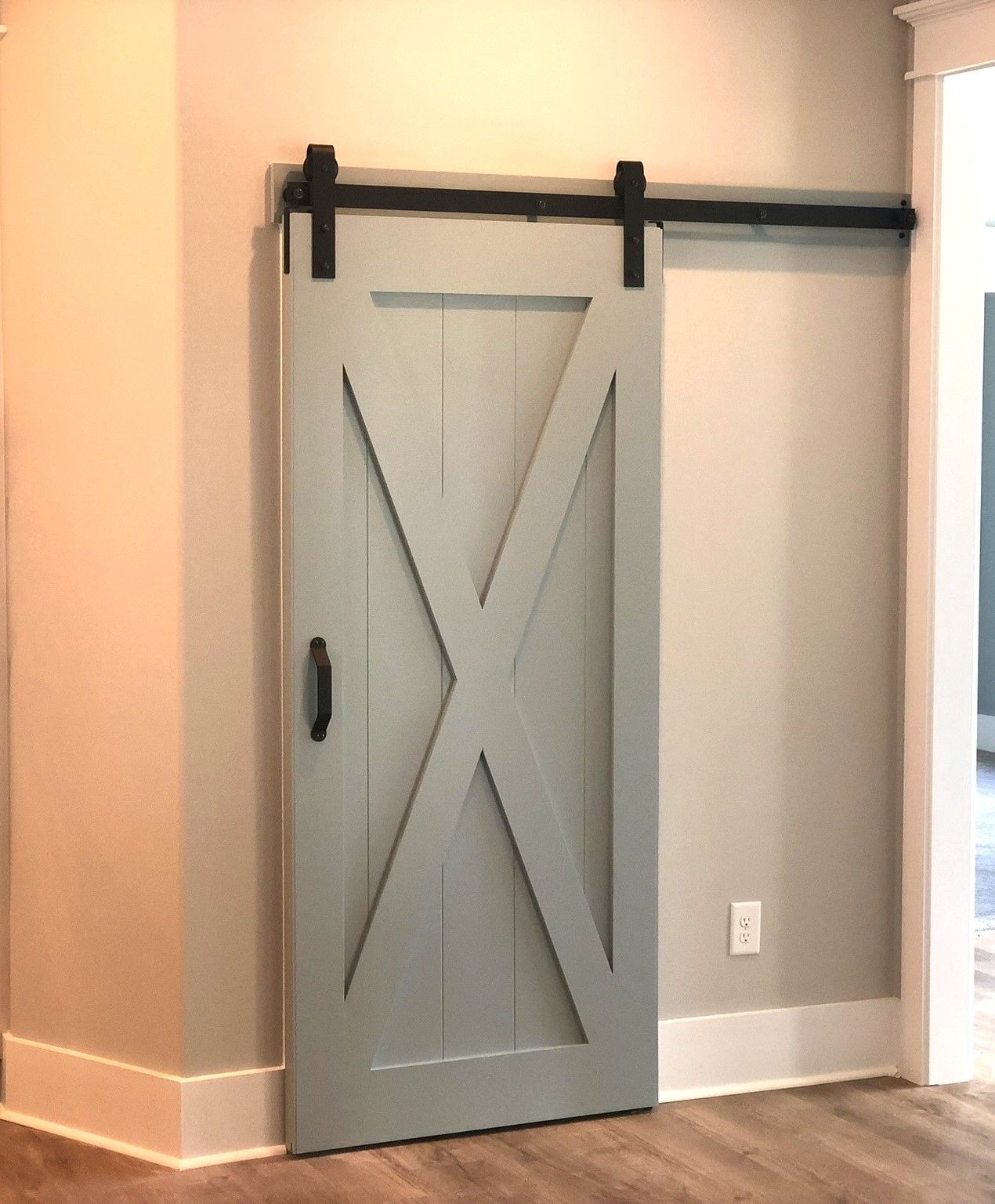 Gray barn door with black hardware and X design, mounted on wall with a black track.