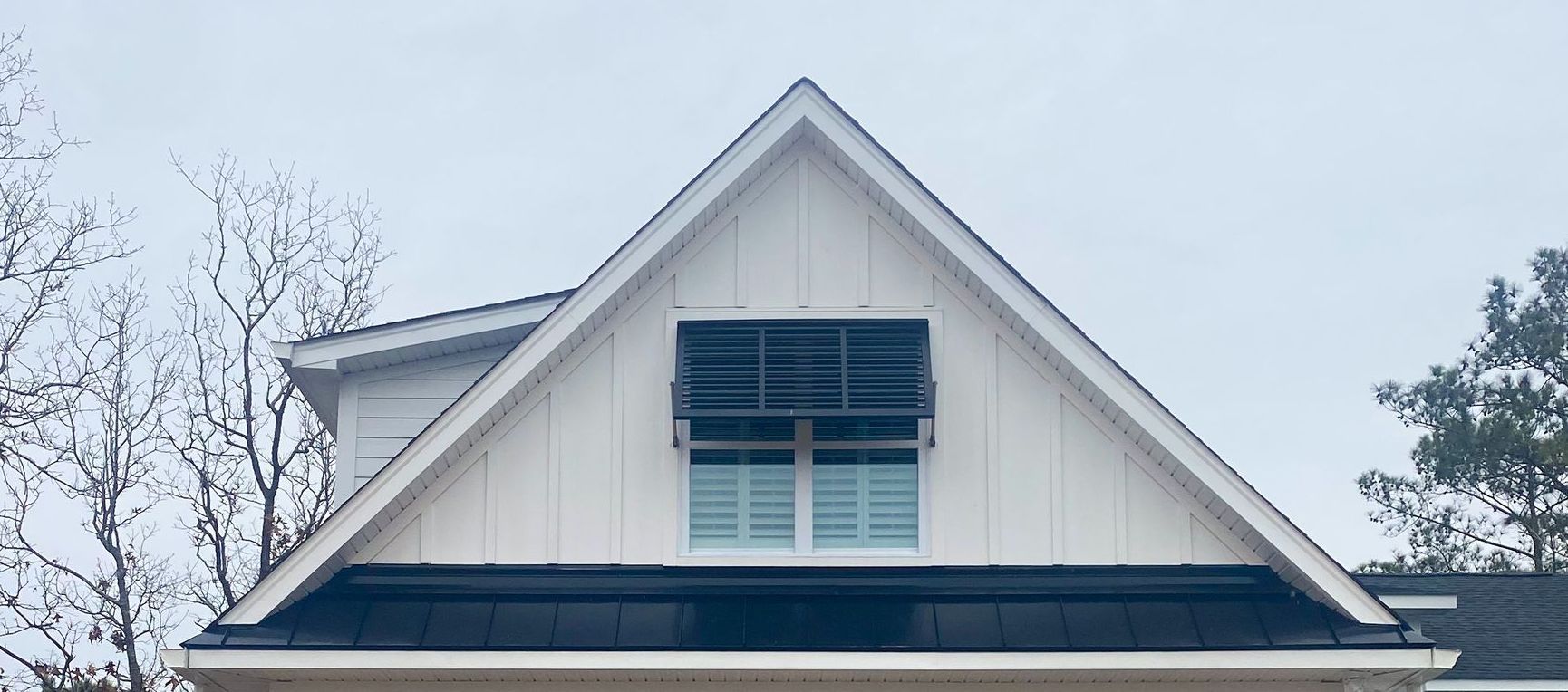 White gable roof with black awning over a window, set against a cloudy sky.