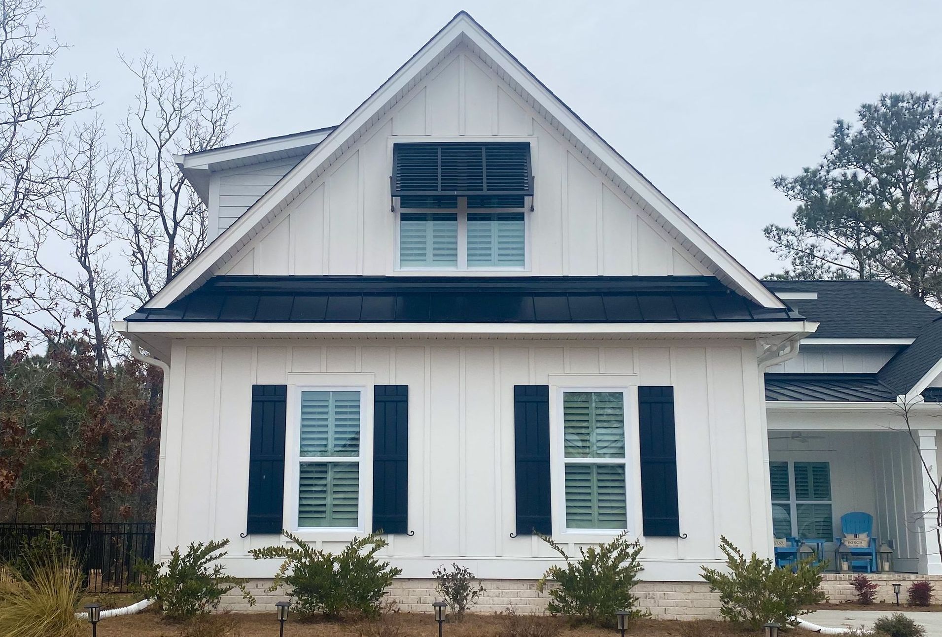 White house with black shutters and awning; blue chairs on porch.