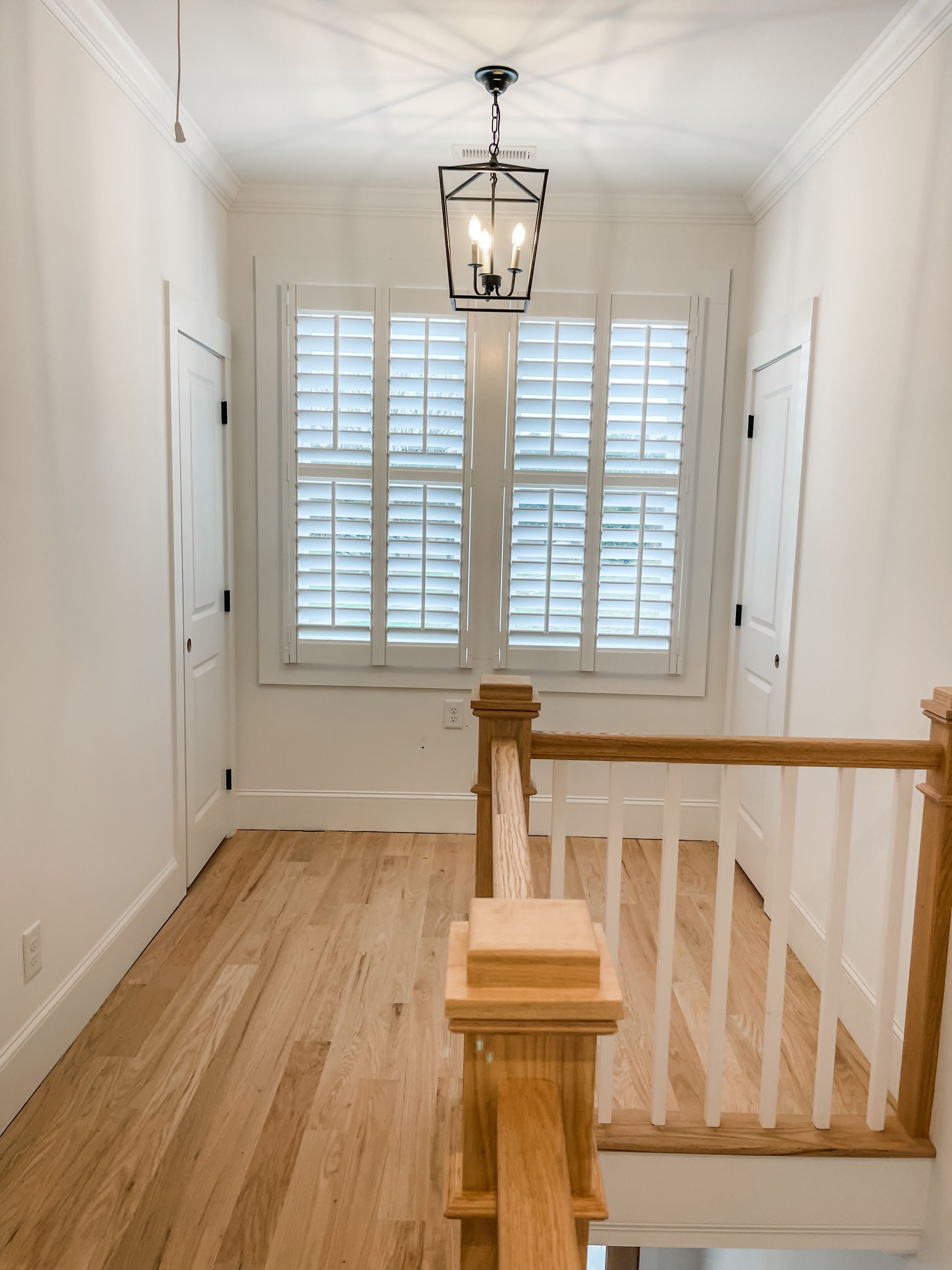 Hallway with hardwood floors, a window with shutters, and a black lantern light fixture.