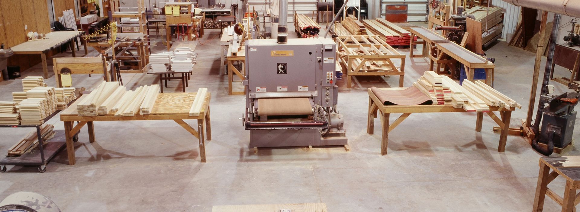 Woodworking shop with large sander, worktables, and lumber.