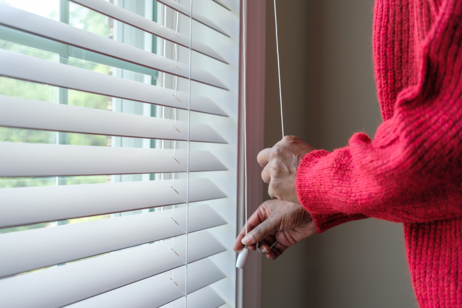 A person opening blinds, enhancing natural light for residential window treatment.