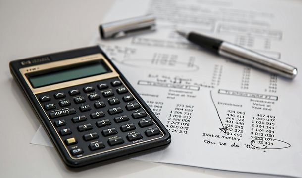 Calculator, pen, and financial documents on a white surface, suggesting accounting or calculations.
