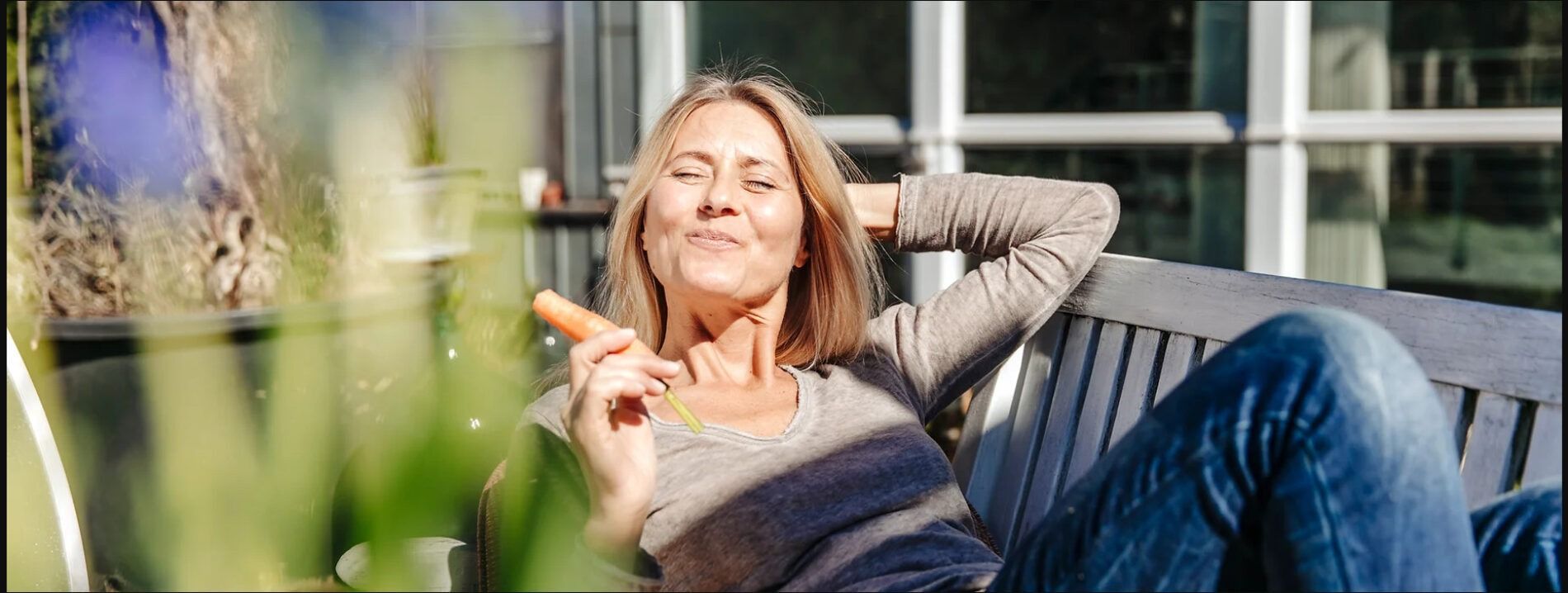 Woman lounging on a bench, holding something, smiling, outdoors.