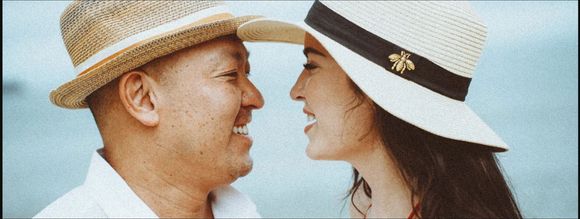 Two people wearing hats, facing each other smiling, with light blue backdrop.