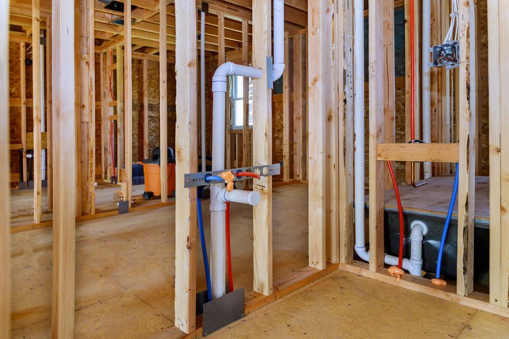 Interior of a room under construction; plumbing pipes and wood framing visible.