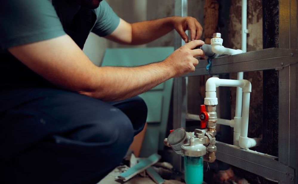 Person installing plumbing; white pipes, blue filter, and red valve.