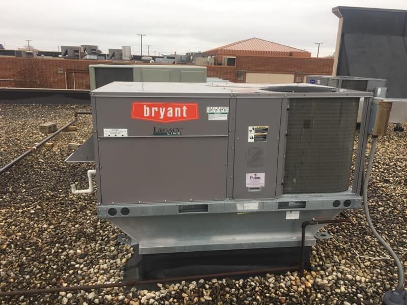 A bryant air conditioner is sitting on top of a gravel covered roof.