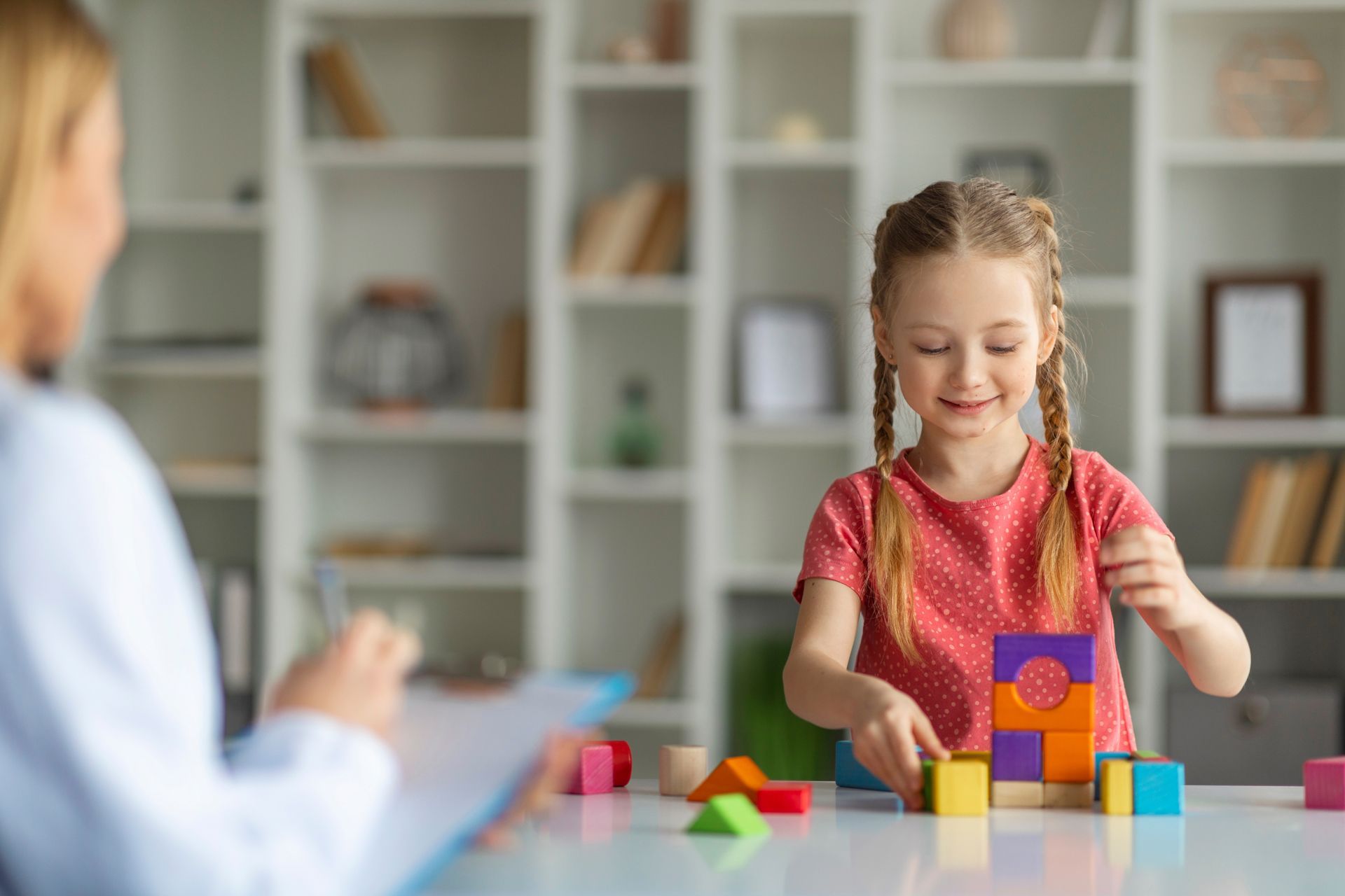 A Little Girl is Sitting at a Table Playing With Wooden Blocks