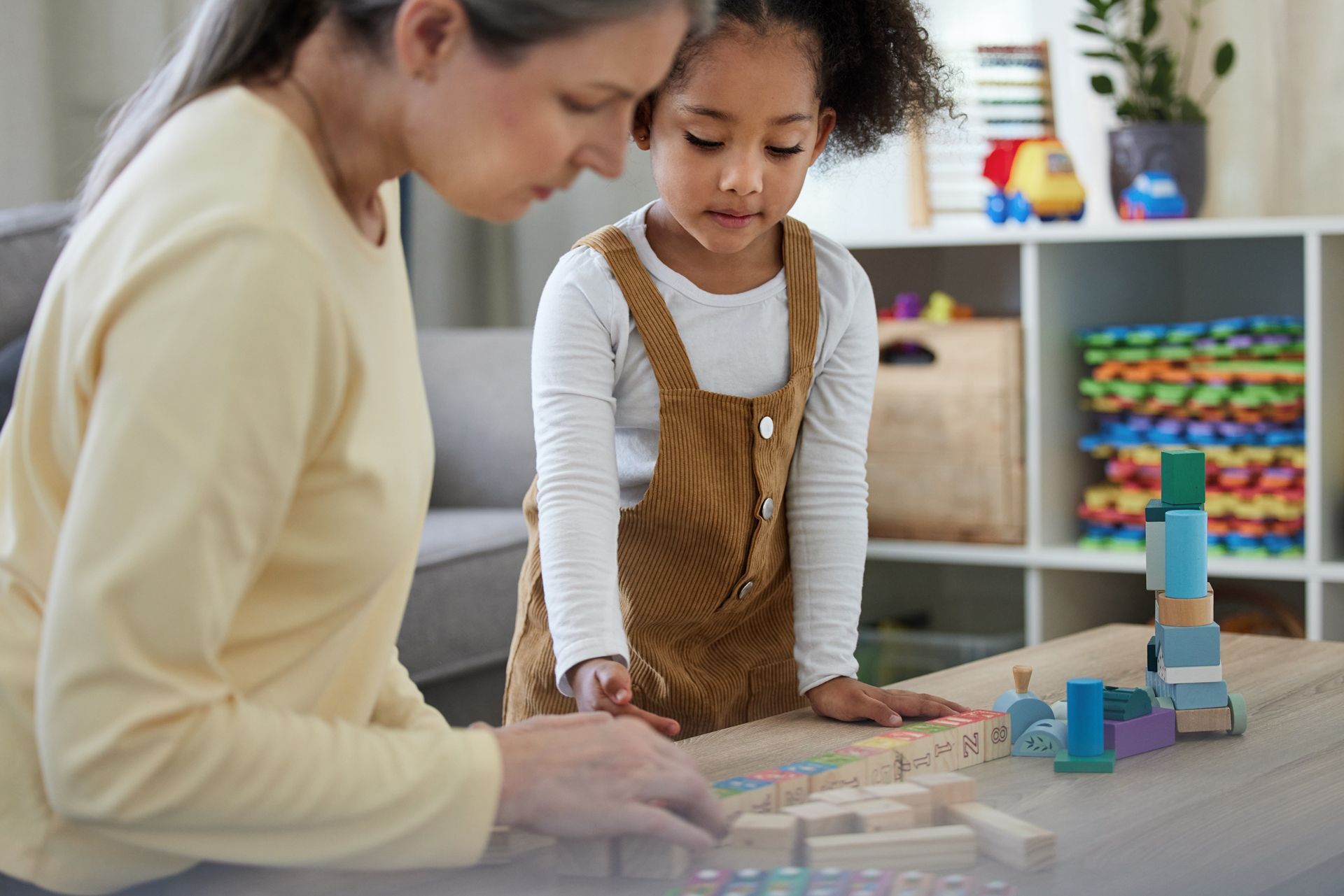 A Woman and a Little Girl Are Playing With Wooden Blocks at a Table