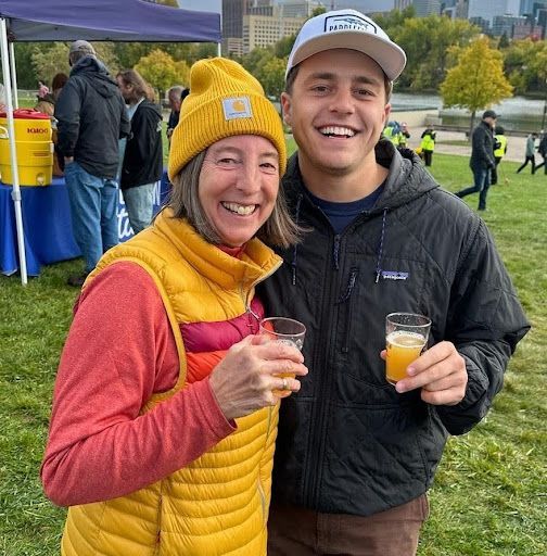 A man and a woman are standing next to each other in a field holding drinks.