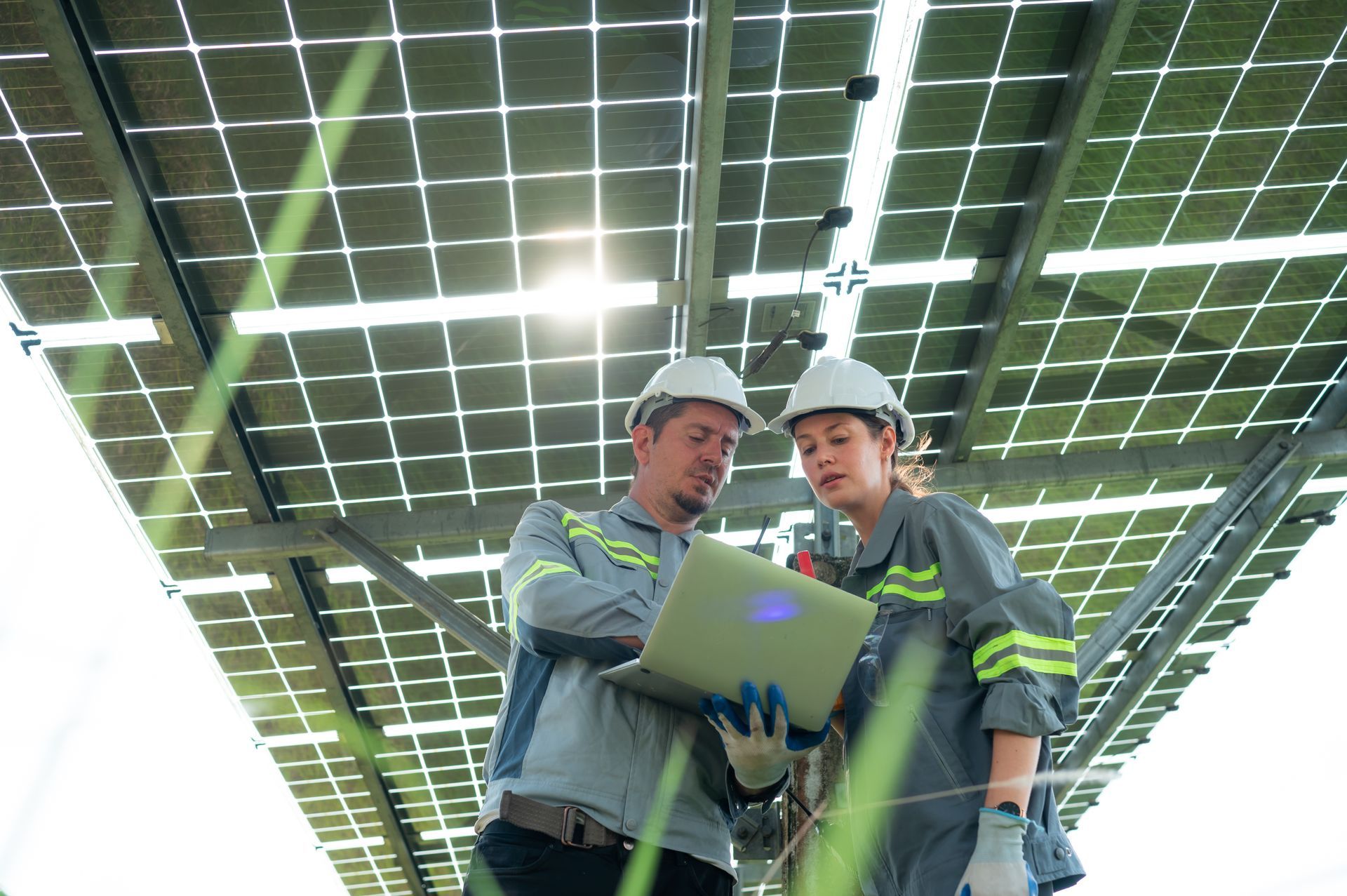 A man and a woman are looking at a laptop in front of a solar panel.