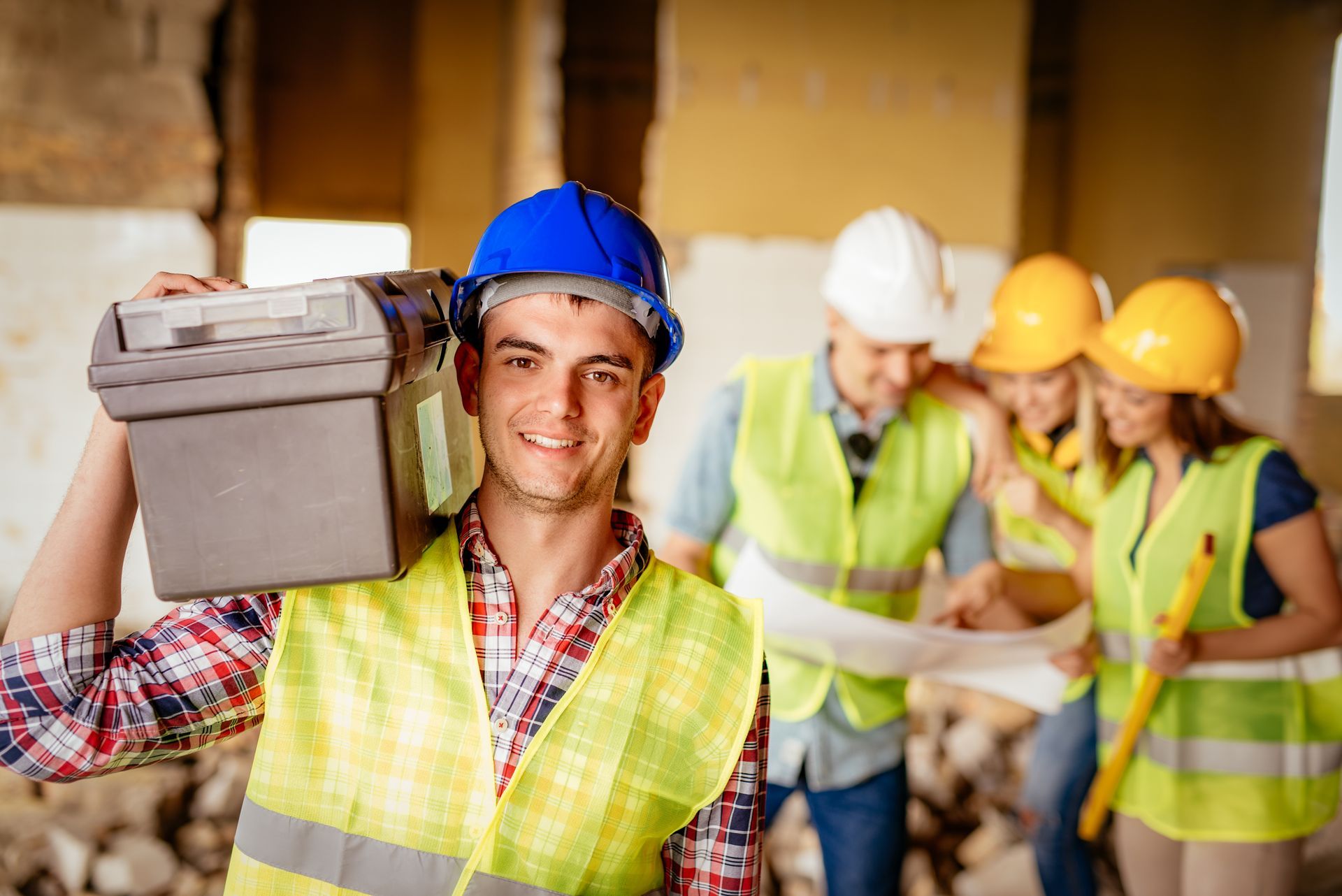 A construction worker is carrying a toolbox on his shoulder.